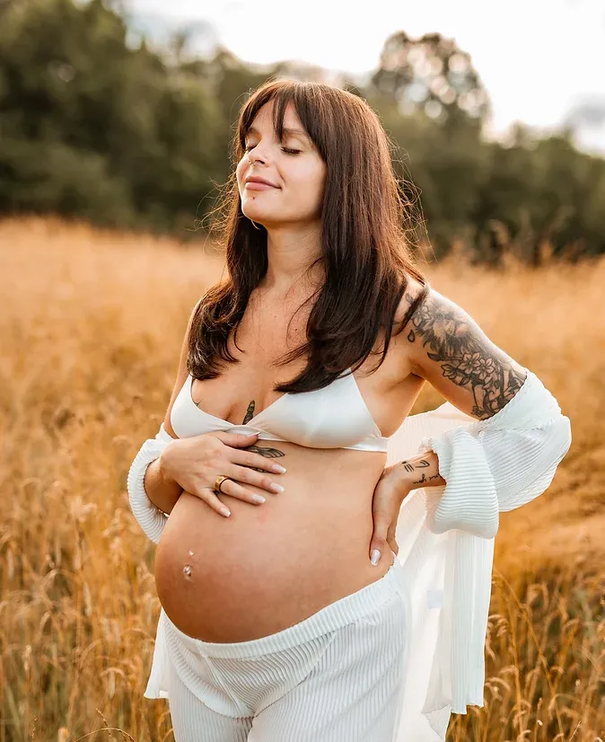 A stunning maternity photo in a golden wheat field at sunset shows an expectant mother in a flowing white dress.