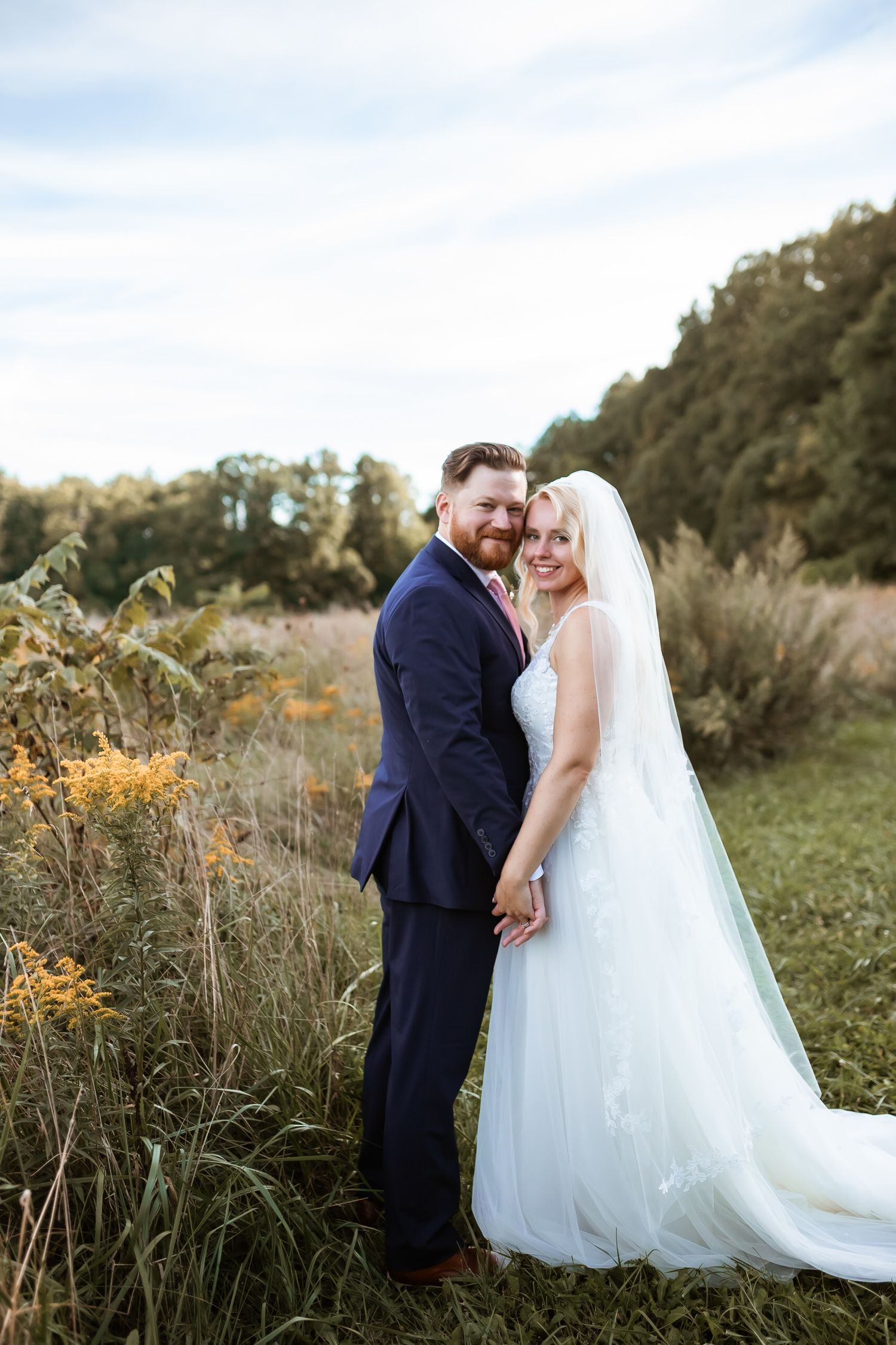 Newlyweds share an intimate moment in a golden field during sunset with bride's veil flowing in the breeze.