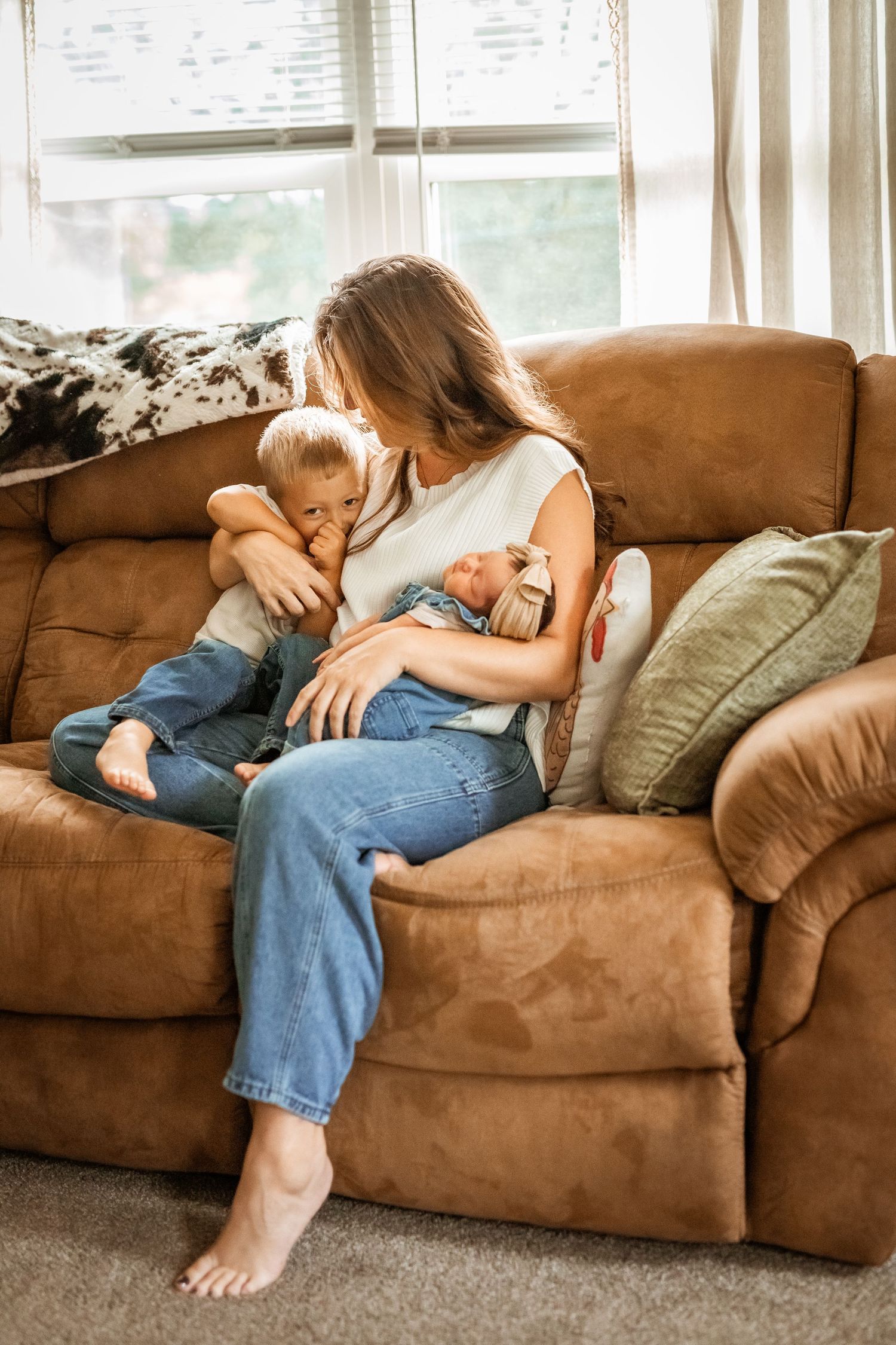 Family snuggling together on a brown couch in a series of candid lifestyle photos showing tender moments.