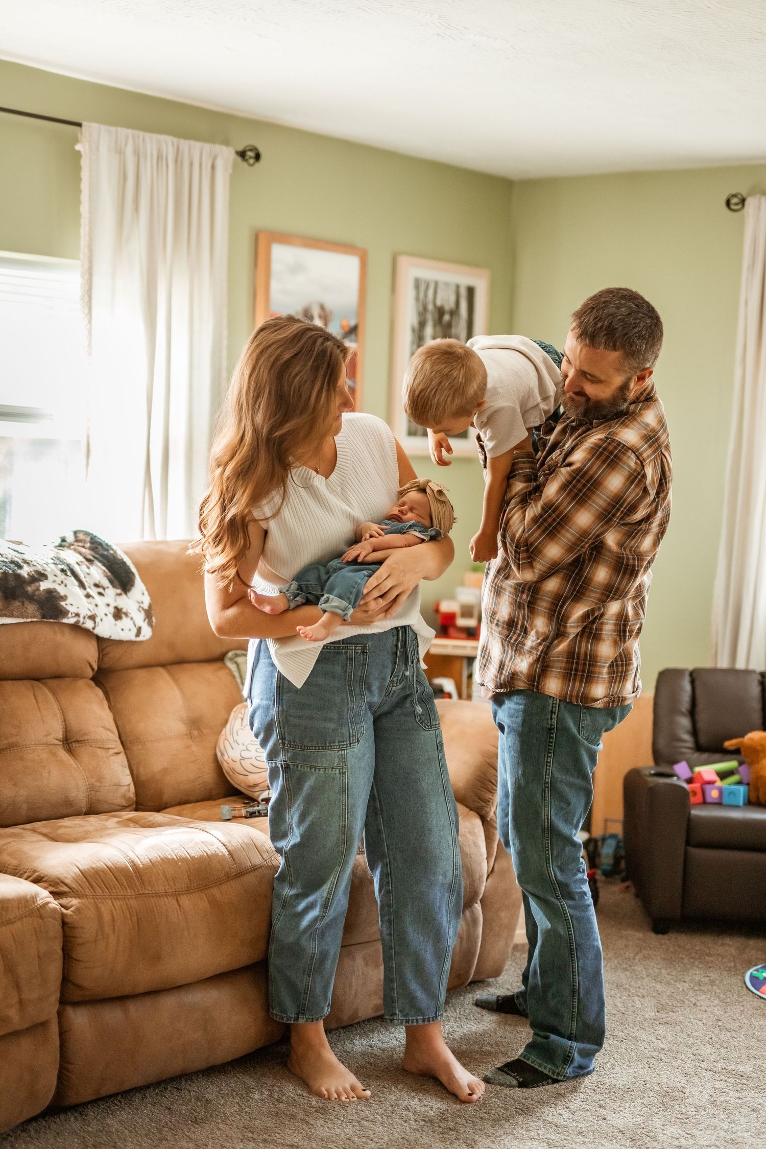 A family plays together in a living room with a brown couch, showing candid moments of interaction and movement.