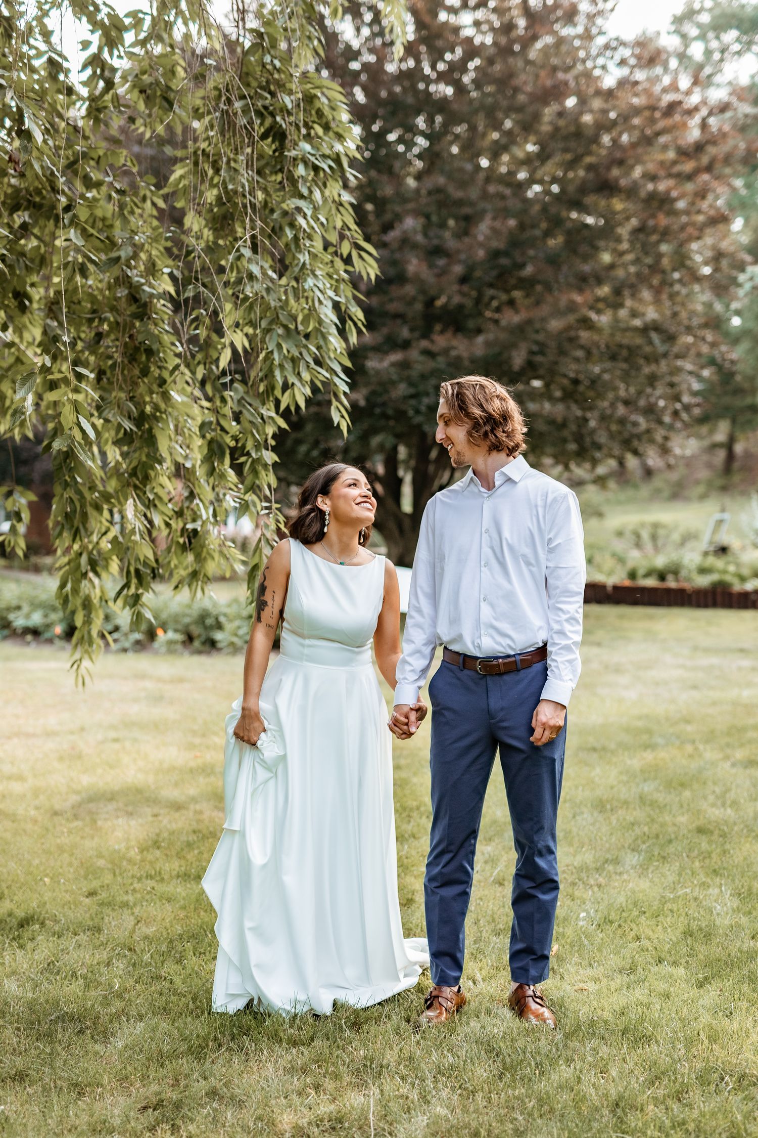 A bride and groom share a joyful moment together on their wedding day under a weeping willow tree in a garden.
