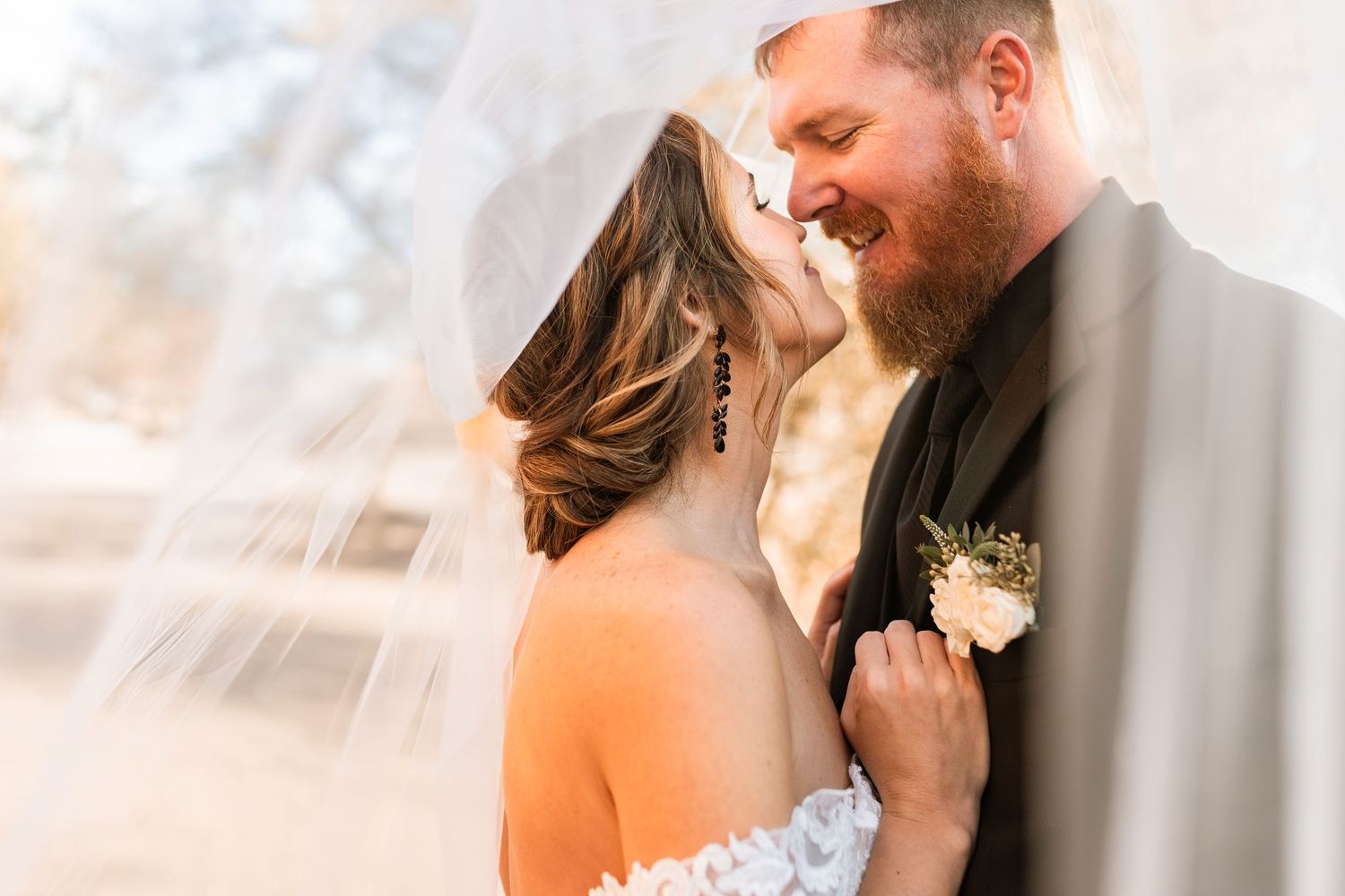 A romantic wedding moment captured through a soft ethereal veil with a white boutonniere accent.