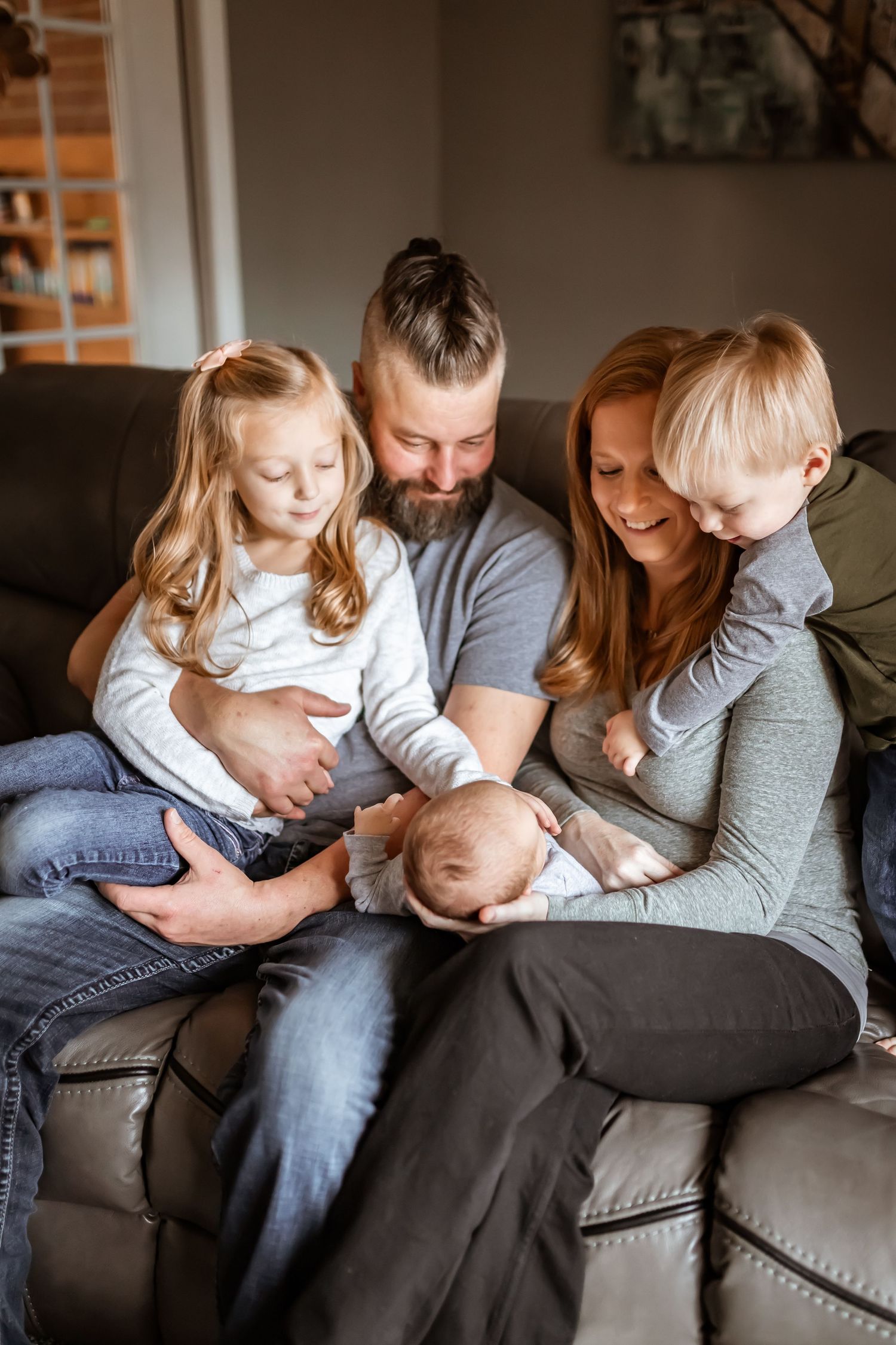 A family gathers on a gray leather couch for an intimate moment with their newborn baby.
