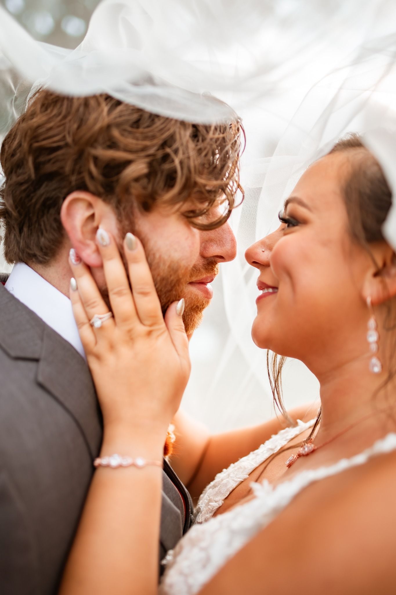 Romantic wedding portrait of couple embracing under flowing white veil.