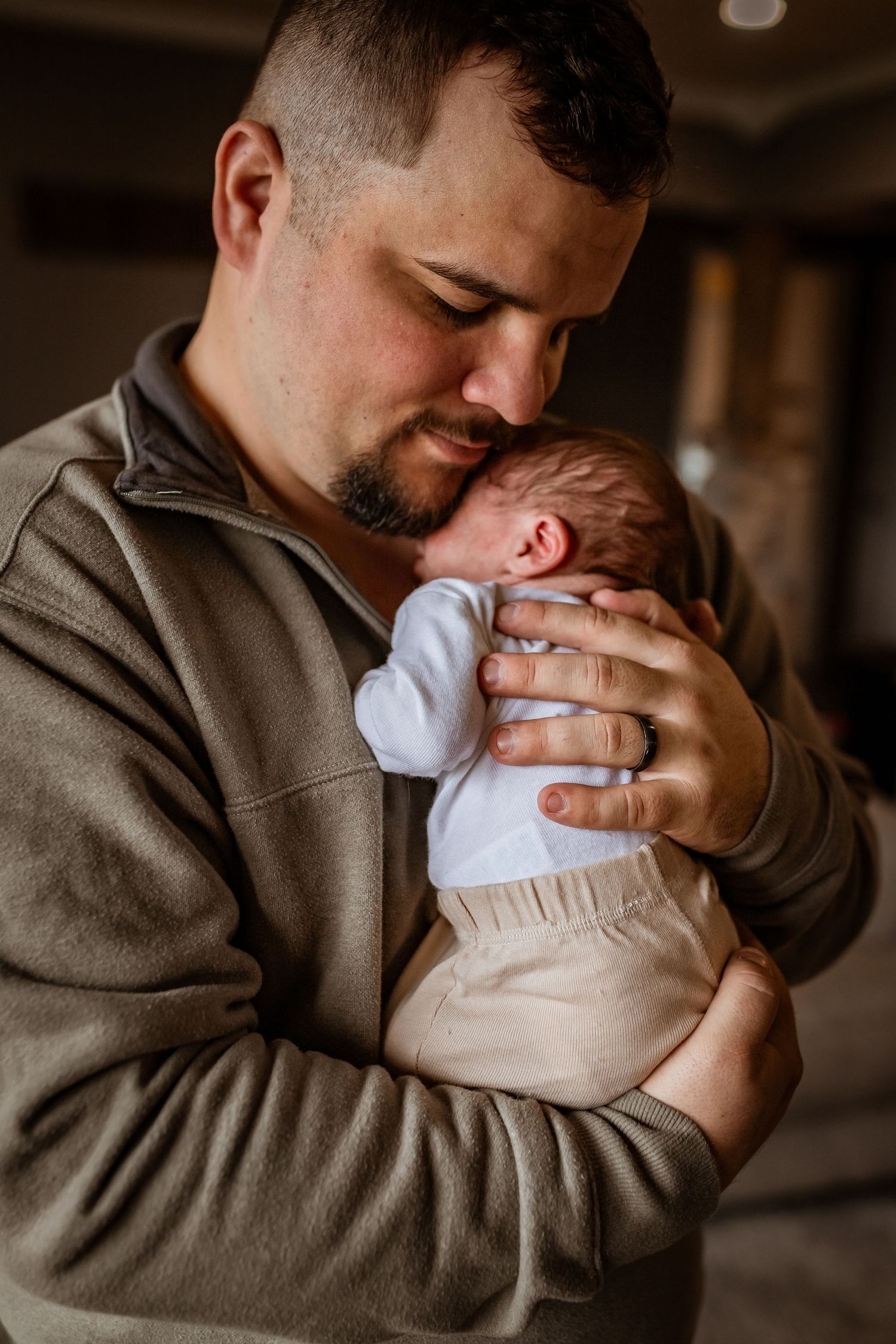A tender moment between a parent wearing a brown hoodie holding and snuggling their sleeping newborn baby.