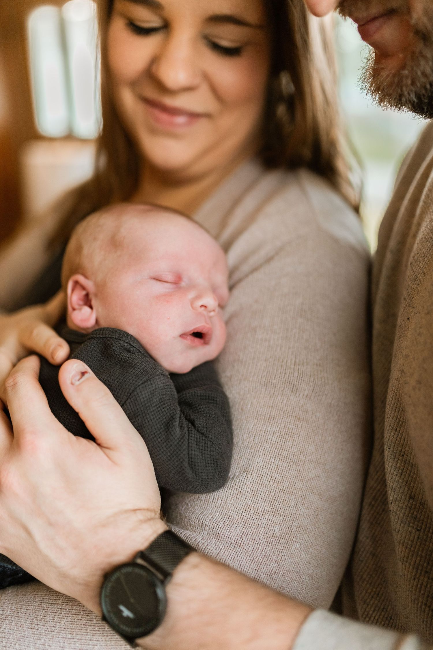 A series of tender moments showing a sleeping newborn baby being cradled in gentle arms wearing a dark gray outfit.