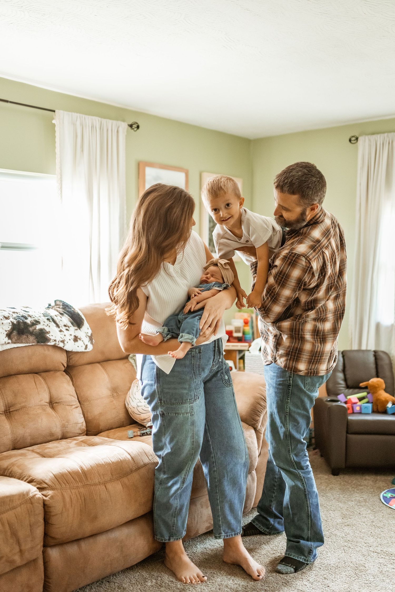 Family in matching denim clothing share playful moments together on a brown couch at home.