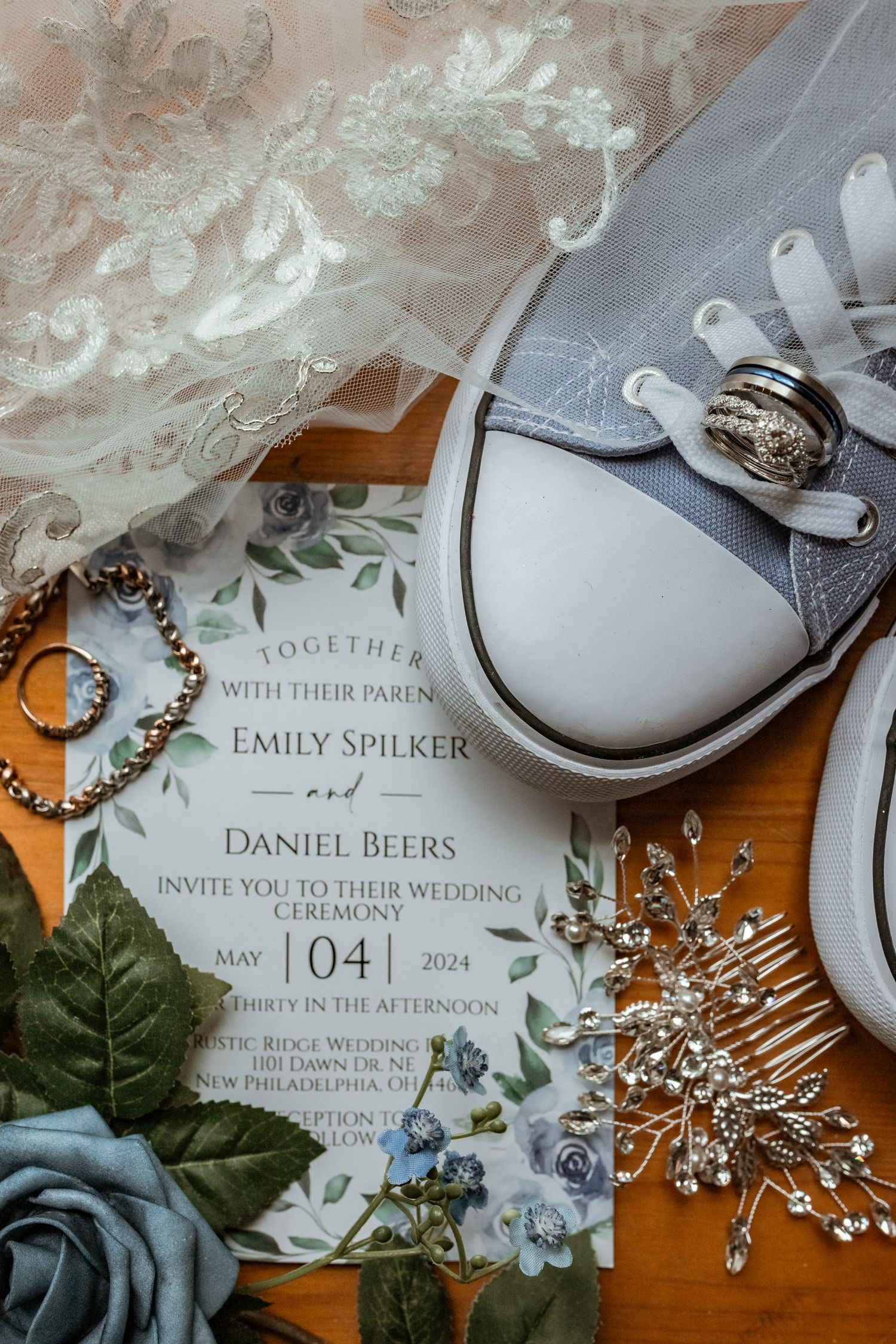 Wedding invitation with gray sneakers, rings, and floral decorations arranged on orange background.