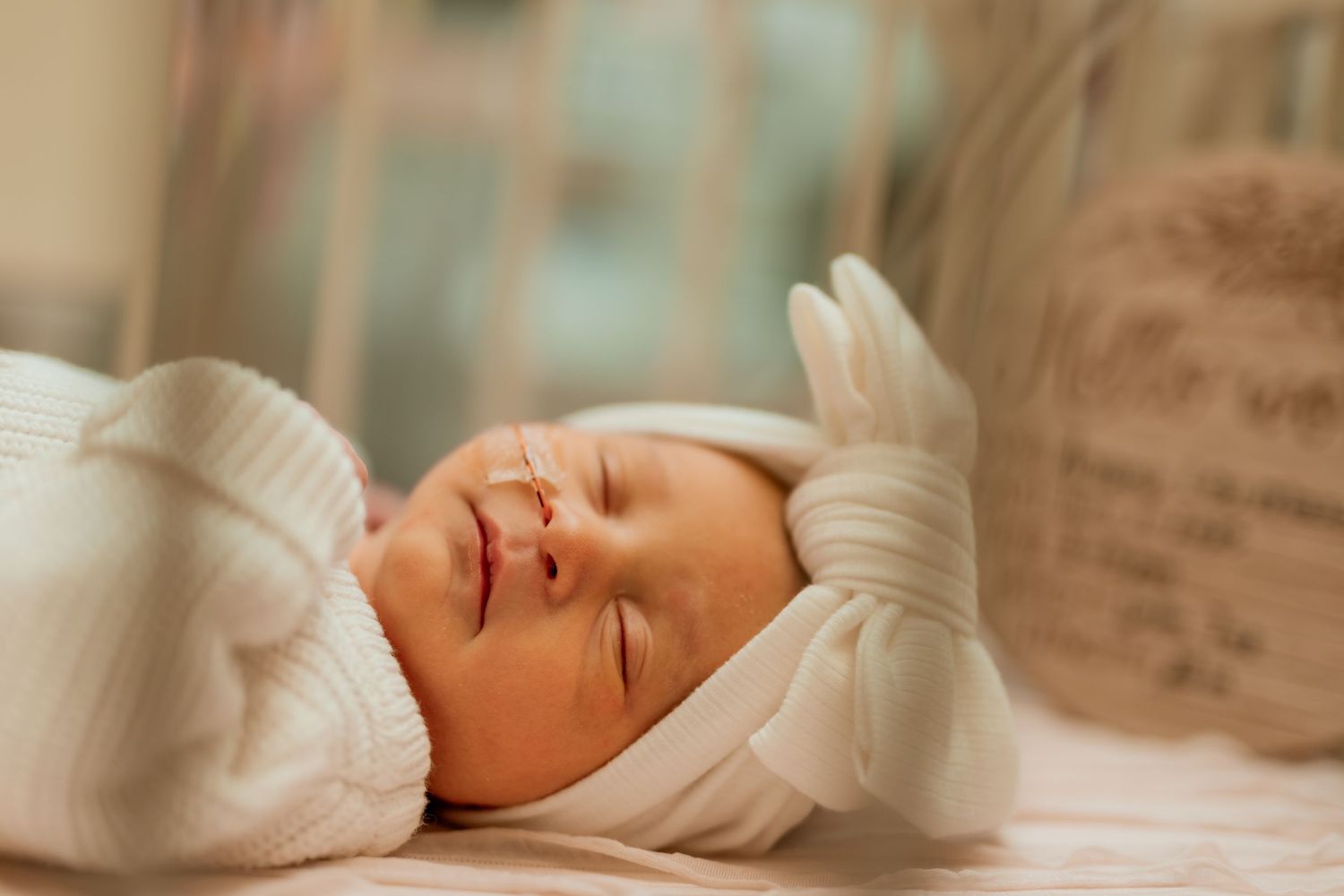 A newborn baby sleeps peacefully in white swaddle blanket in soft window light.