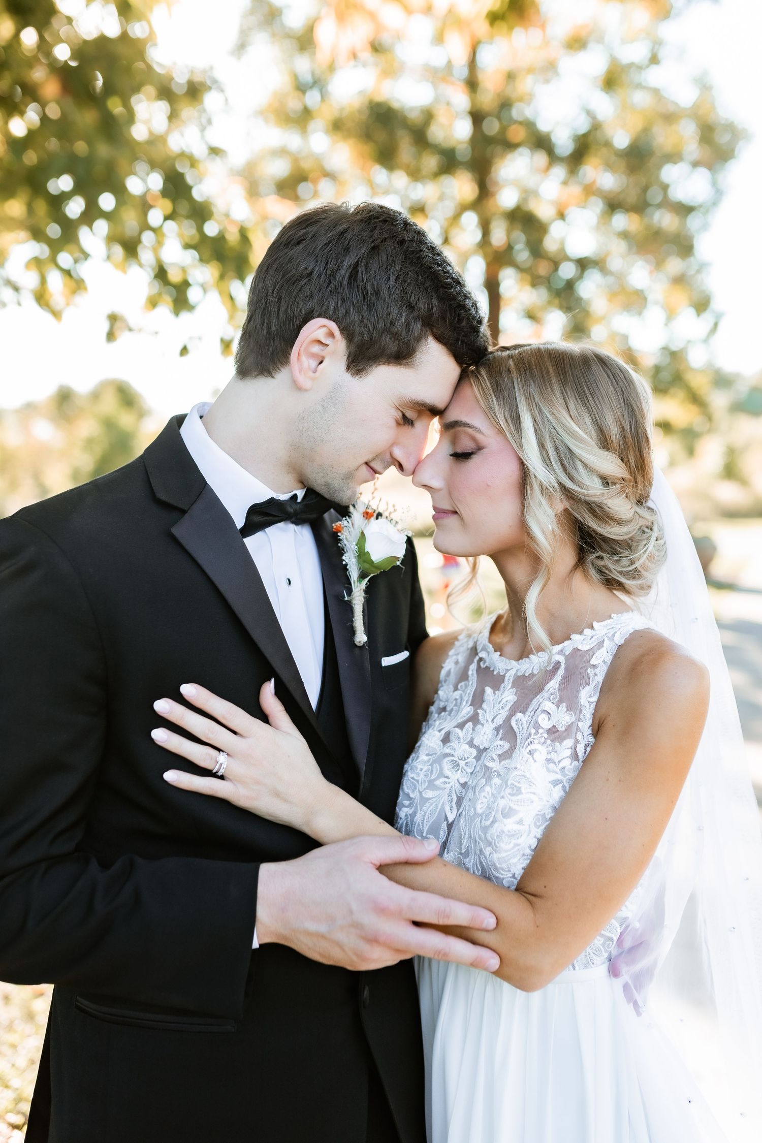 Newlywed couple in formal attire share an intimate moment outdoors with autumn leaves in background.