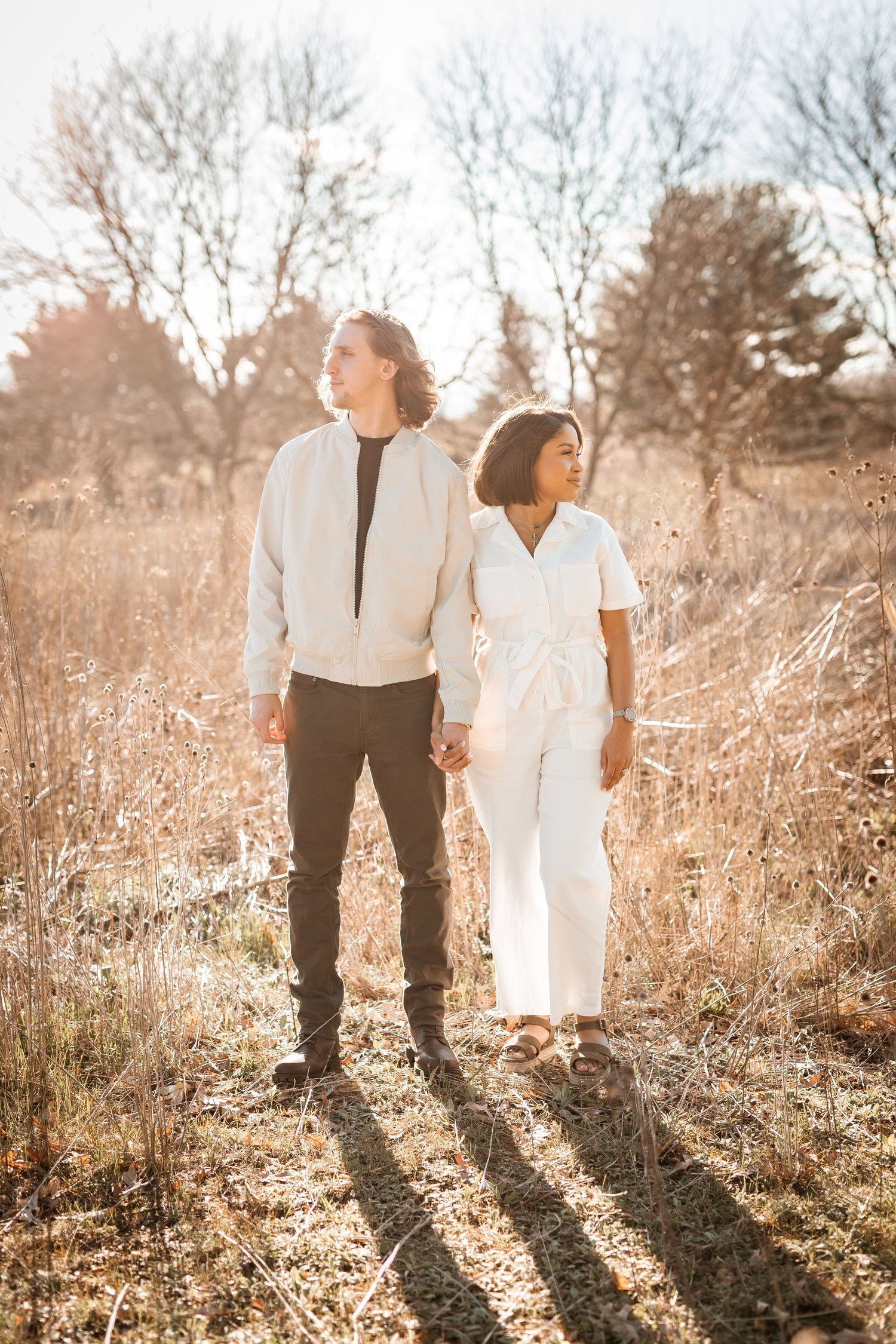 Couple in white outfits standing in a sunlit autumn field during golden hour.