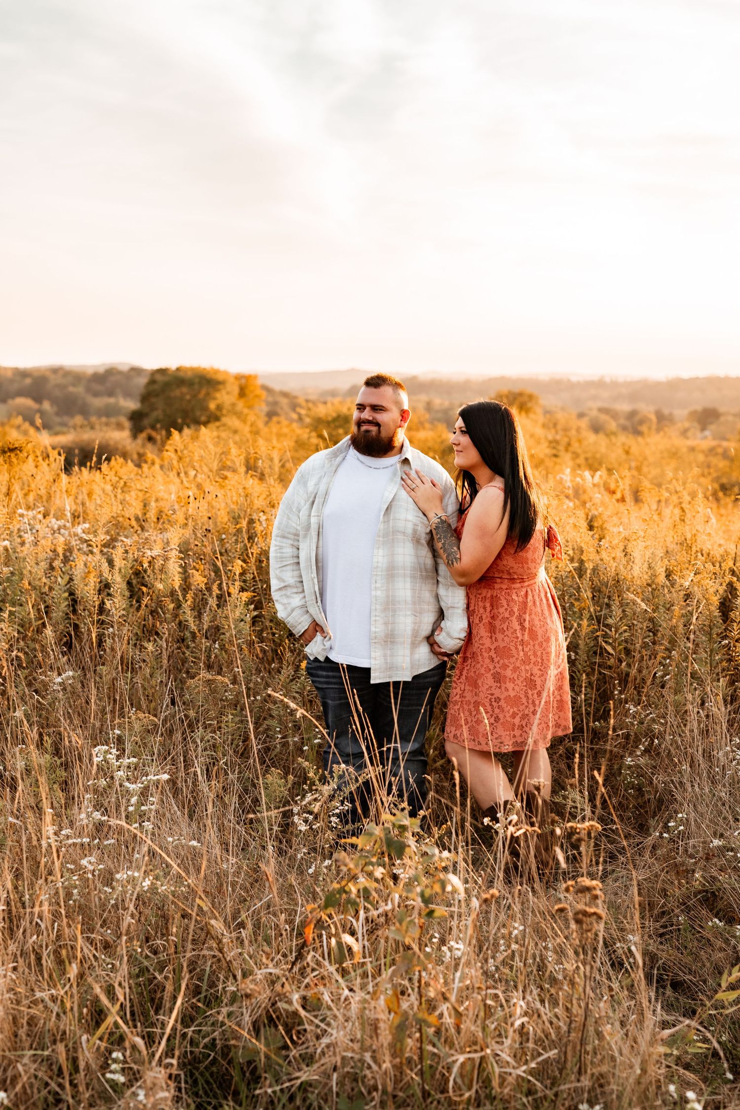 A couple shares an intimate moment at sunset in a golden wheat field on an autumn evening.