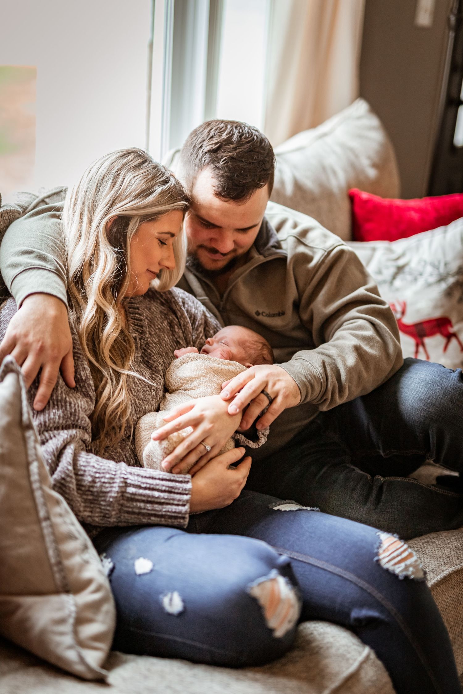 Couple sits on cozy couch cuddling their newborn baby during an intimate lifestyle photography session.