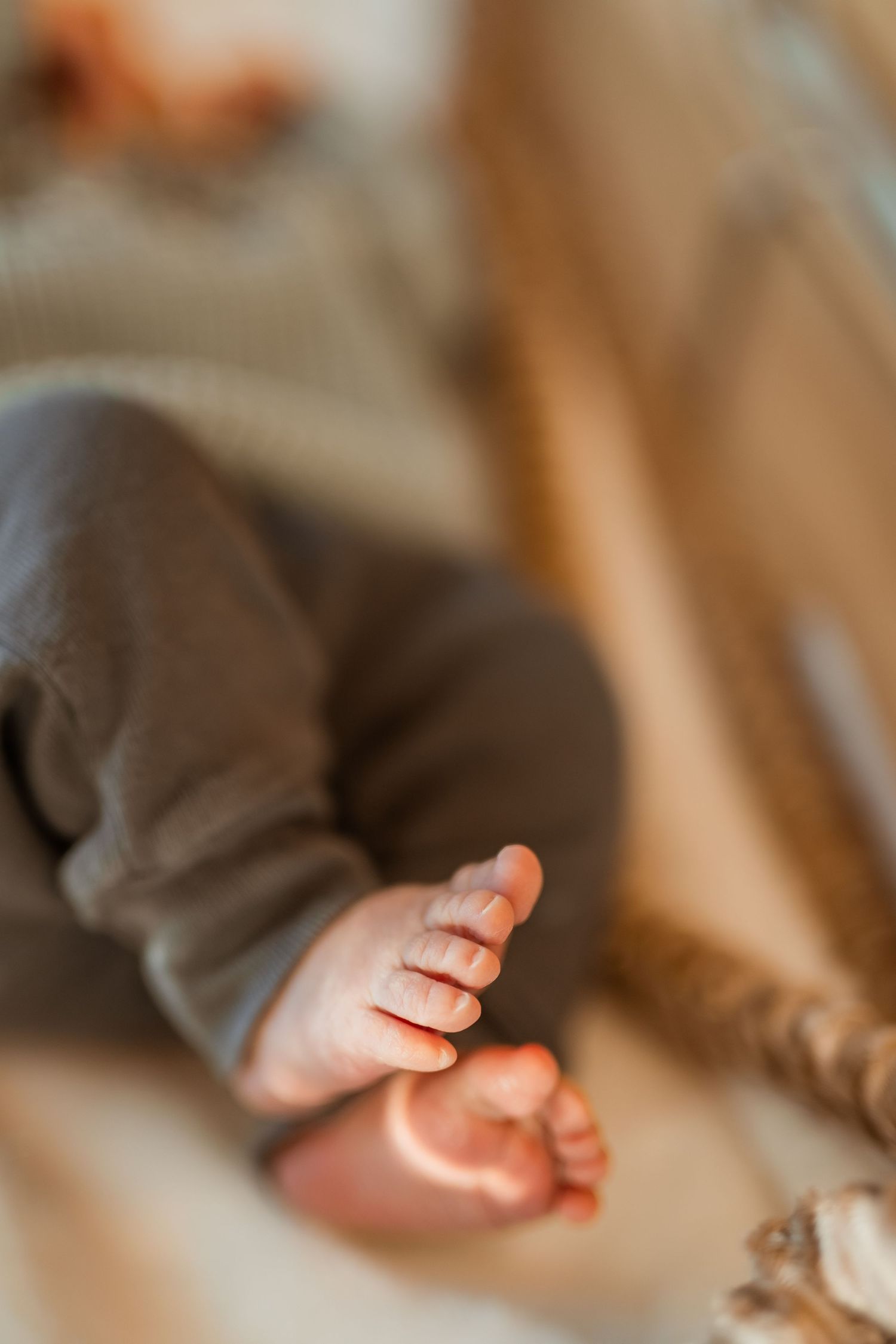 Close-up view of tiny baby feet with gray pants in soft, warm lighting on cozy bedding.