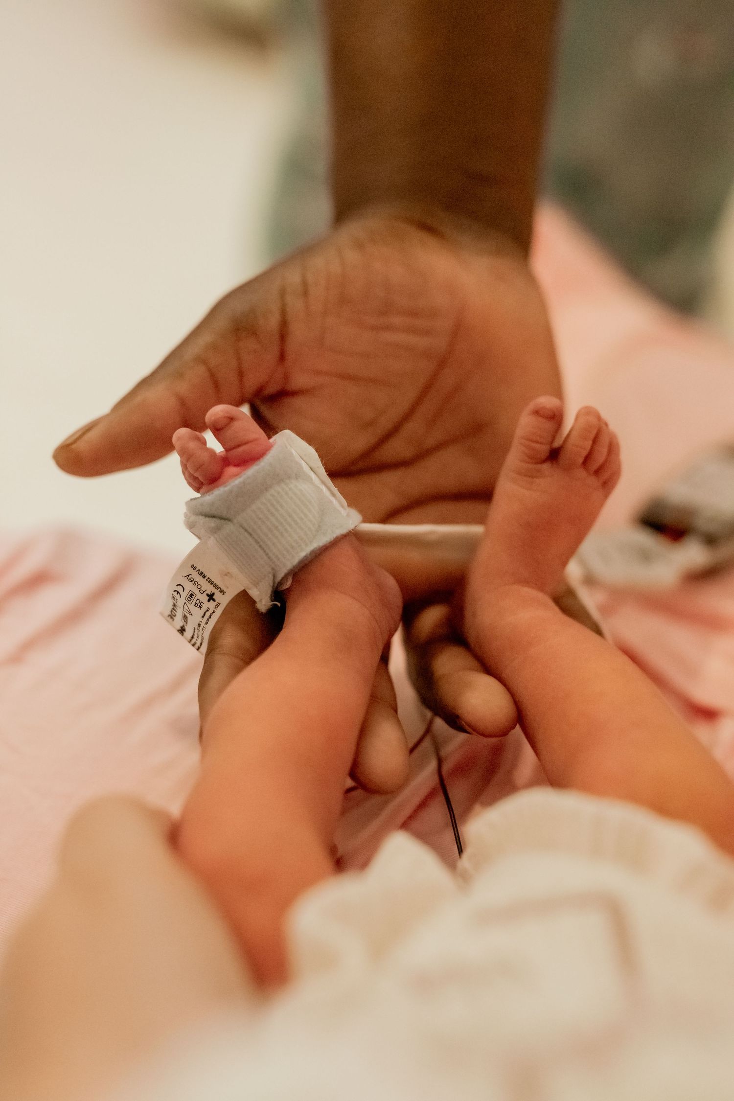 A tiny newborn's foot being held by an adult hand with a hospital ID bracelet on the baby's ankle.