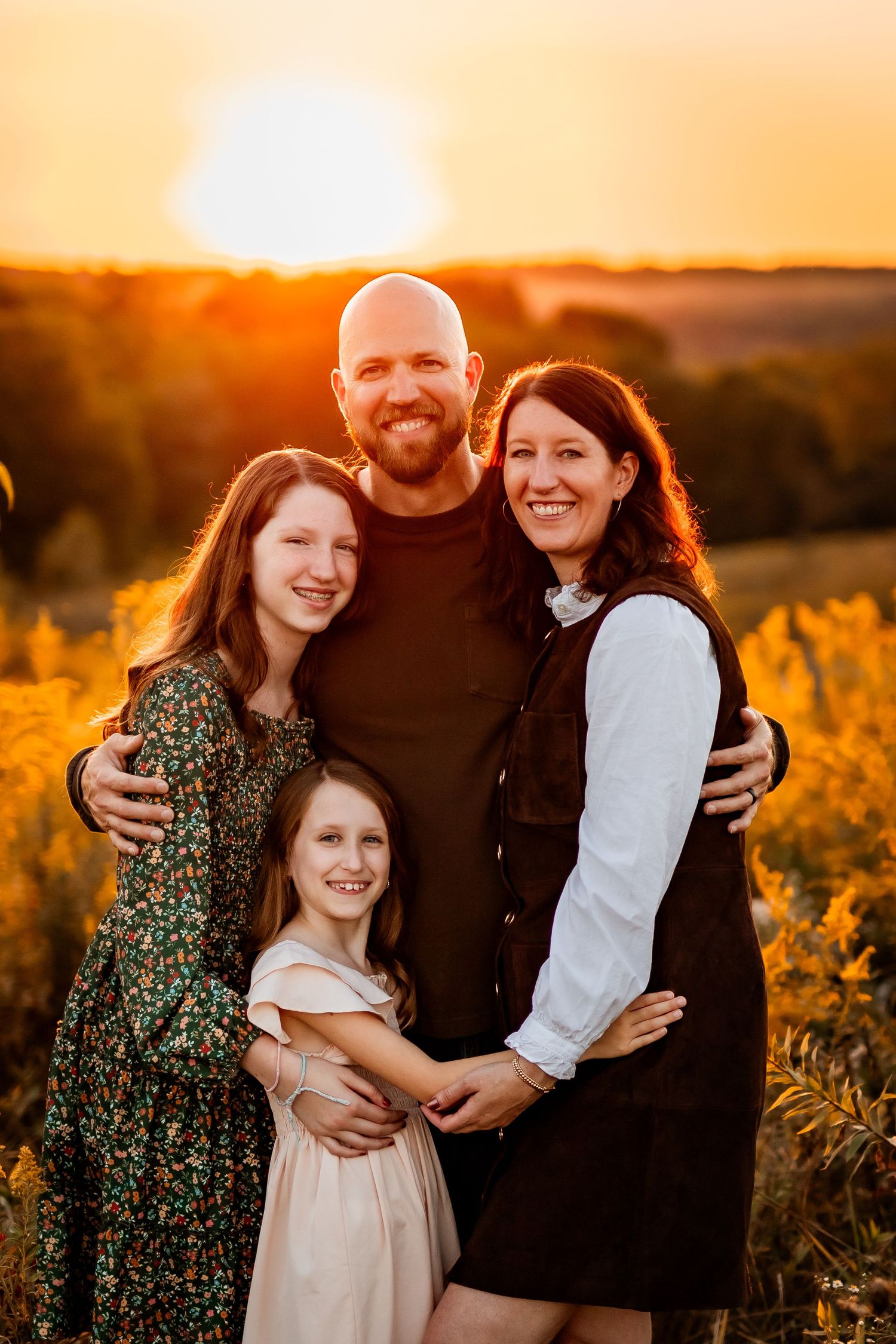 A family poses together in a field at sunset with golden light illuminating the scene.