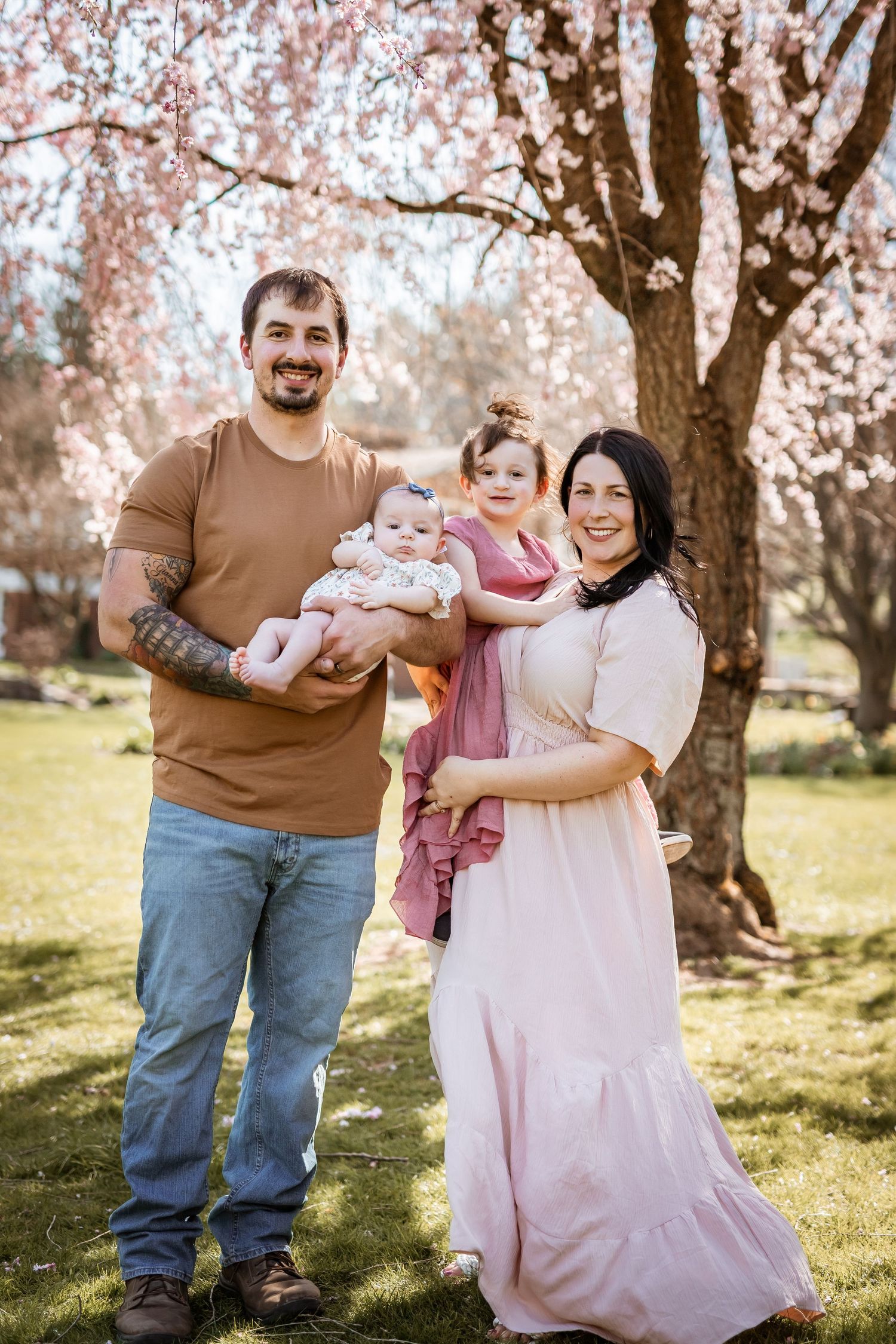 A family stands together under blooming cherry blossom trees on a sunny spring day in the park.