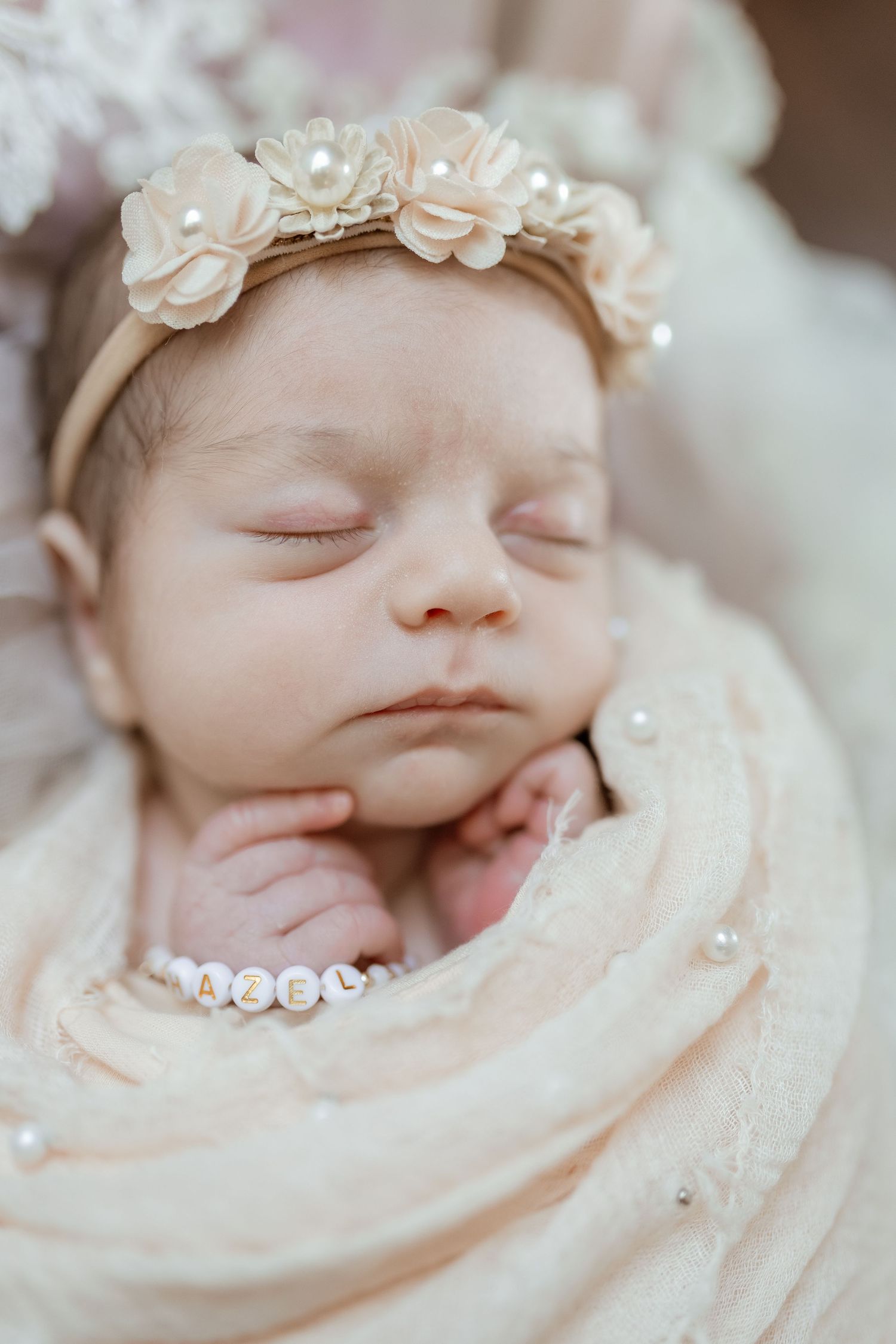 Peaceful newborn sleeping in soft cream wrap with delicate white floral headband.