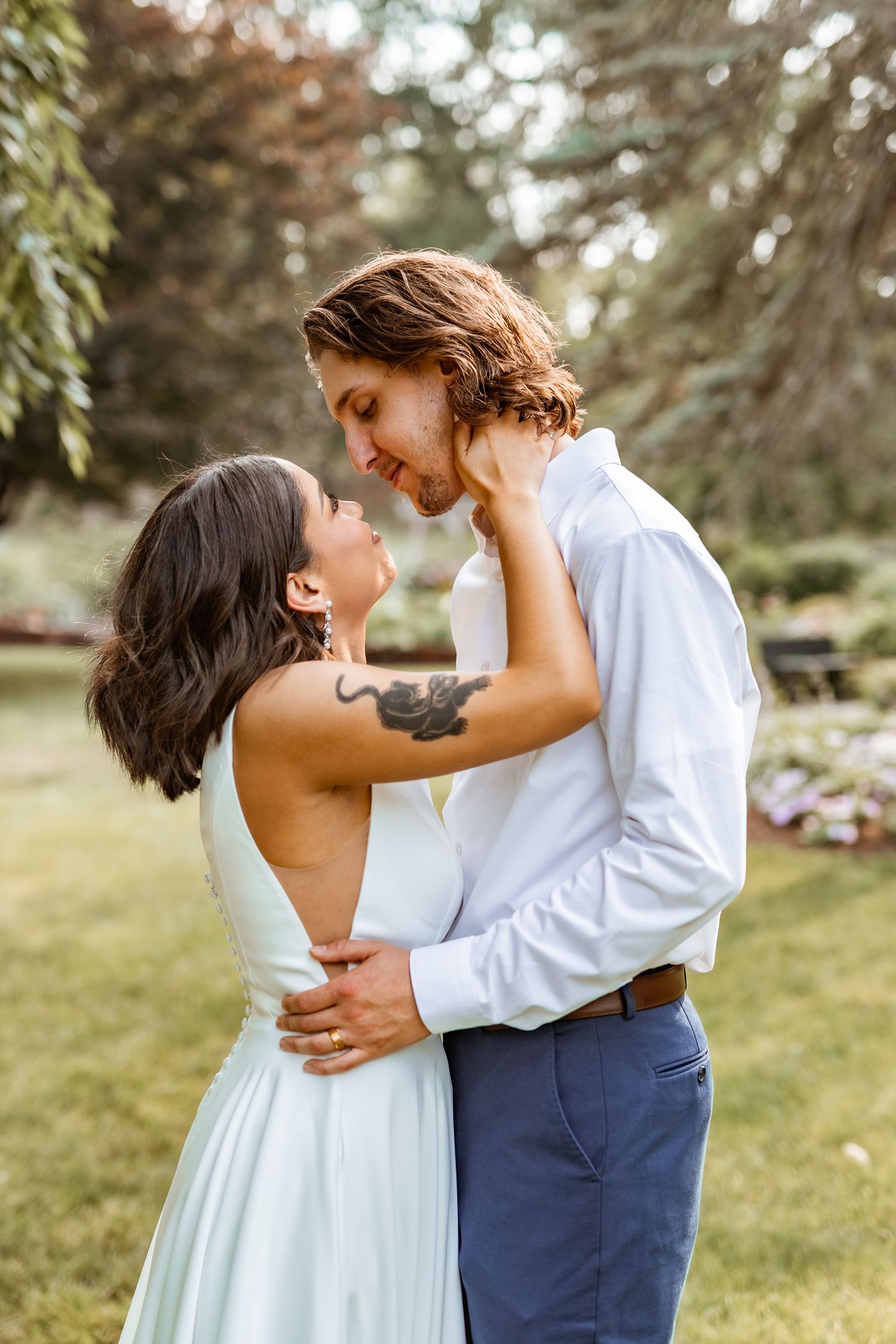 Romantic wedding couple embraces in a garden setting with soft natural lighting during their outdoor celebration.