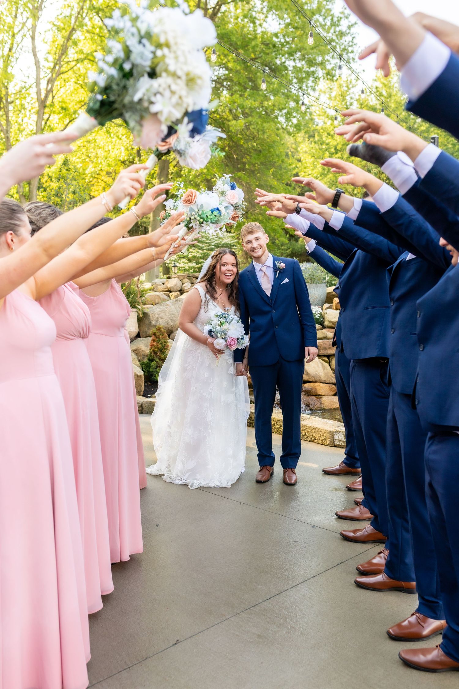 Newlyweds walk through an arch of raised hands formed by bridesmaids and groomsmen outdoors.