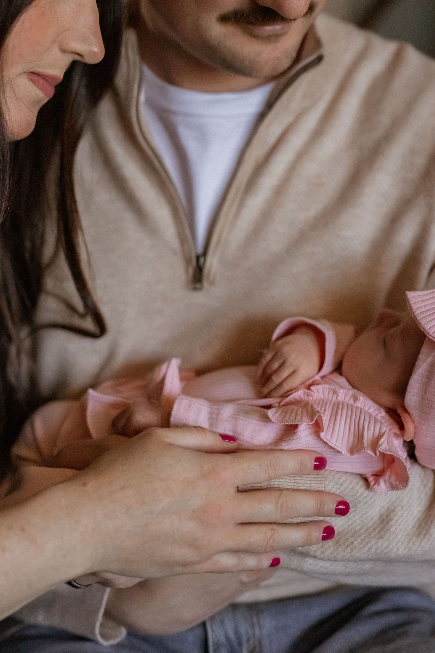 Parents cradling their newborn baby dressed in pink, a tender moment captured in a cozy indoor setting.