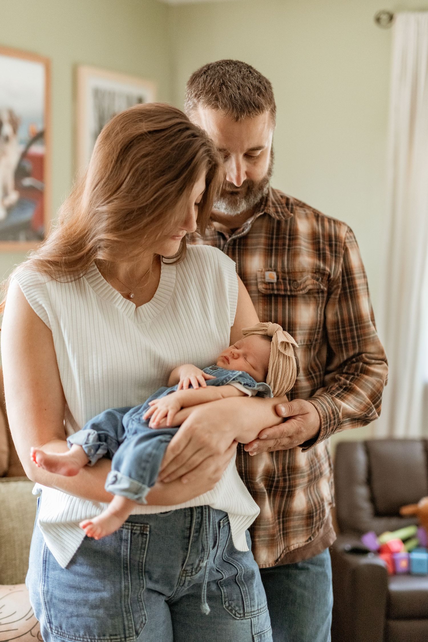 A couple shares tender moments with their newborn baby in a living room setting with natural lighting.