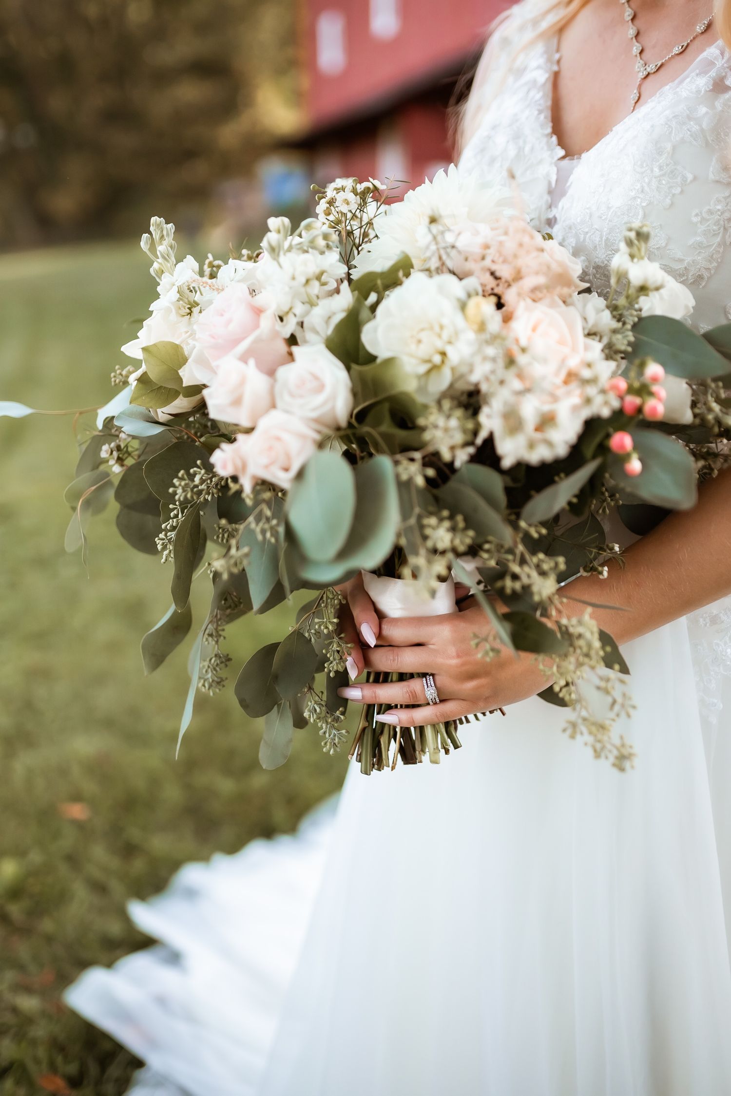 Elegant bridal bouquet featuring blush pink and white flowers with eucalyptus leaves against a white wedding dress.