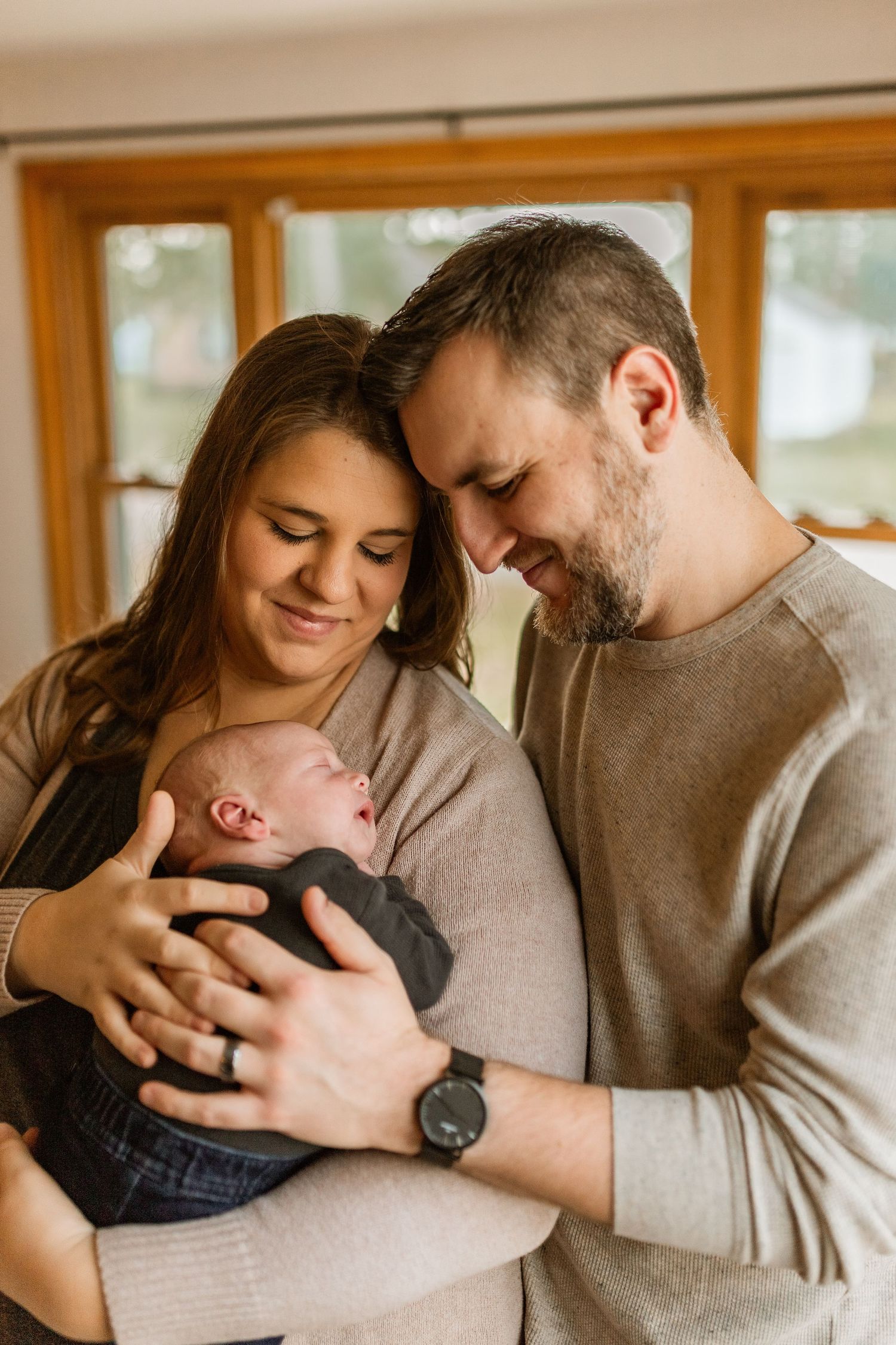 A loving couple holds and gazes adoringly at their newborn baby in a series of tender moments by a window.