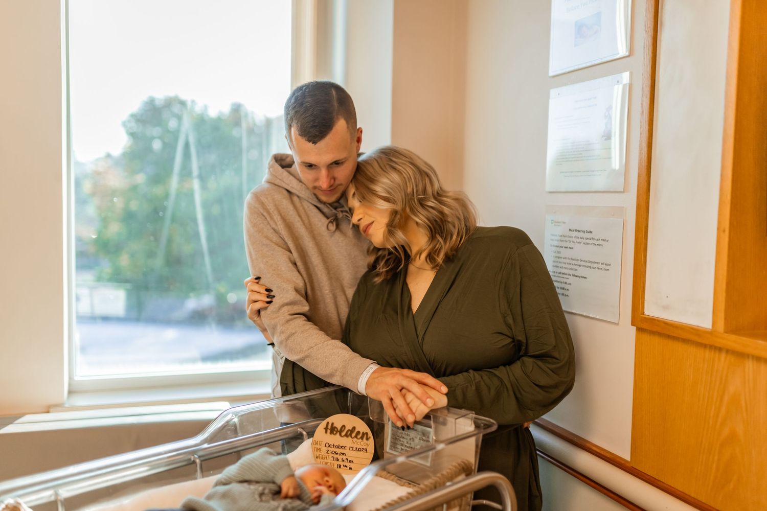 A couple shares an intimate moment together while preparing food in a sunlit kitchen by a window.