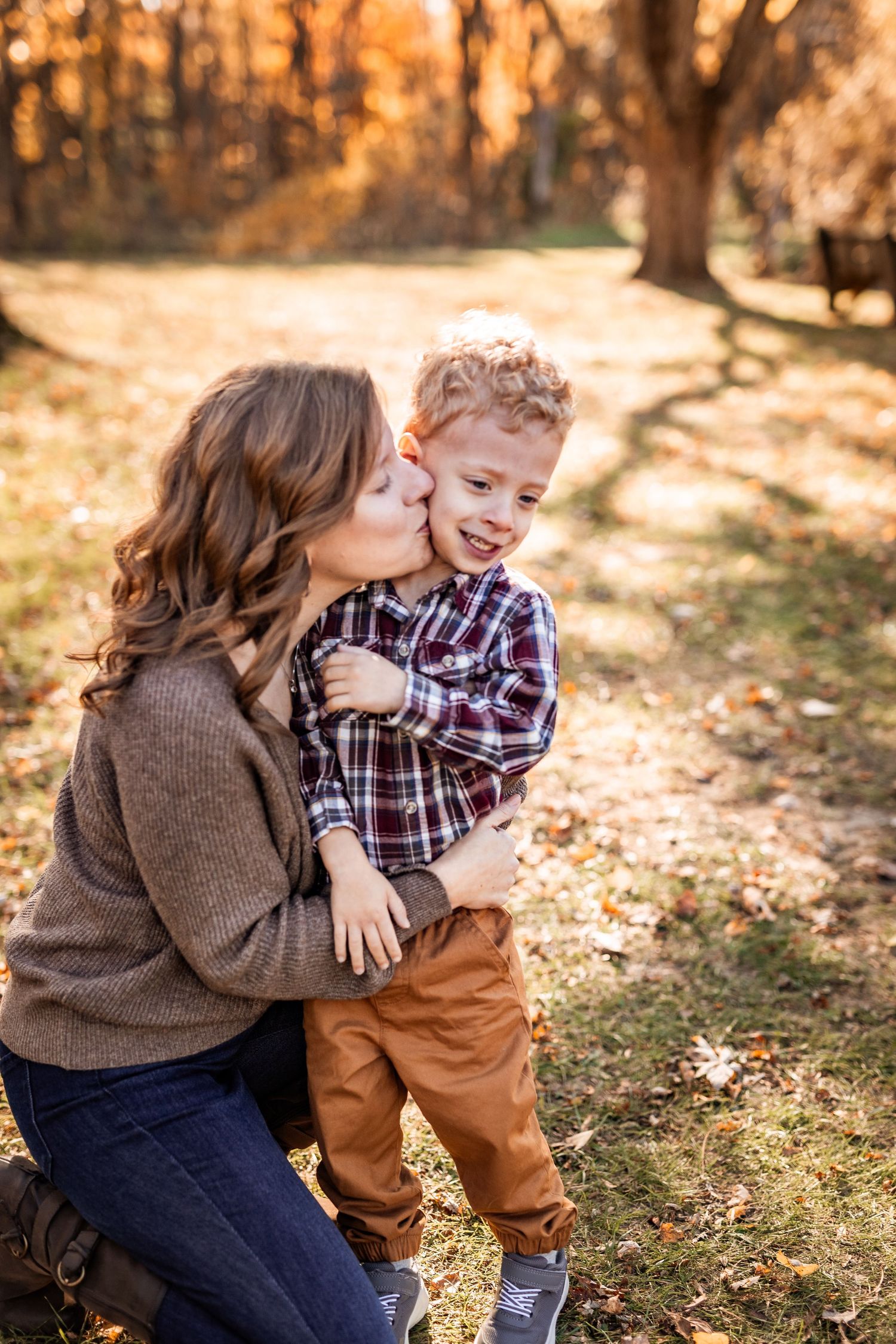 A sweet autumn moment captured in golden sunlight as fallen leaves scatter around a pair sharing an affectionate moment outdoors.