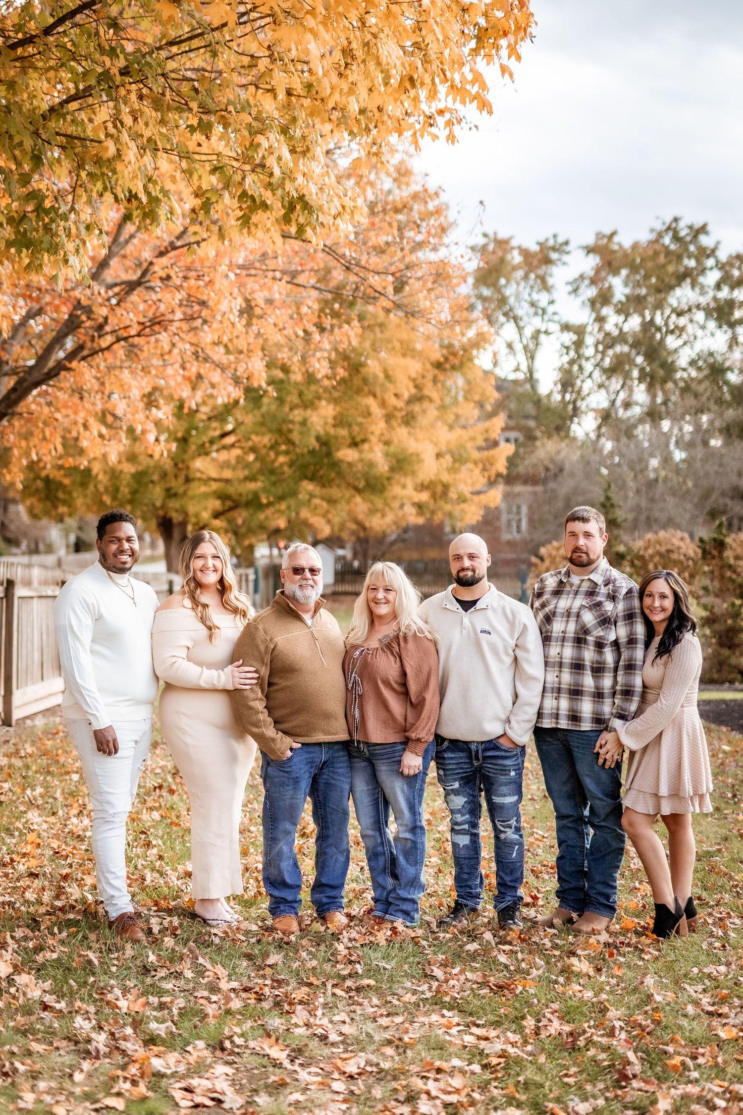 A group of people stand together outdoors in coordinated fall outfits surrounded by autumn foliage.