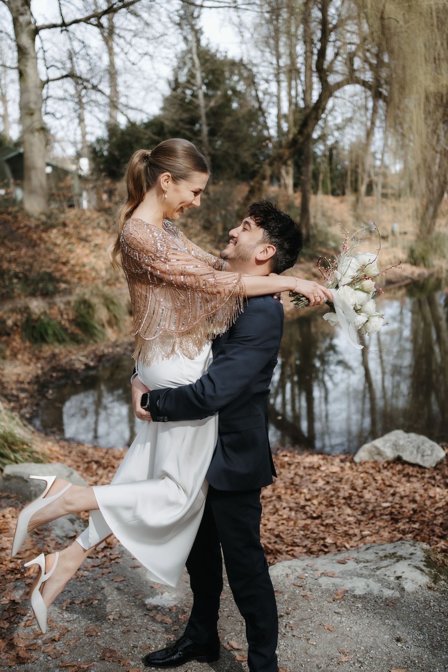 Emotionales Foto vom Brautpaar. Die Braut springt in die Arme ihres Mannes und er dreht sich mit ihr