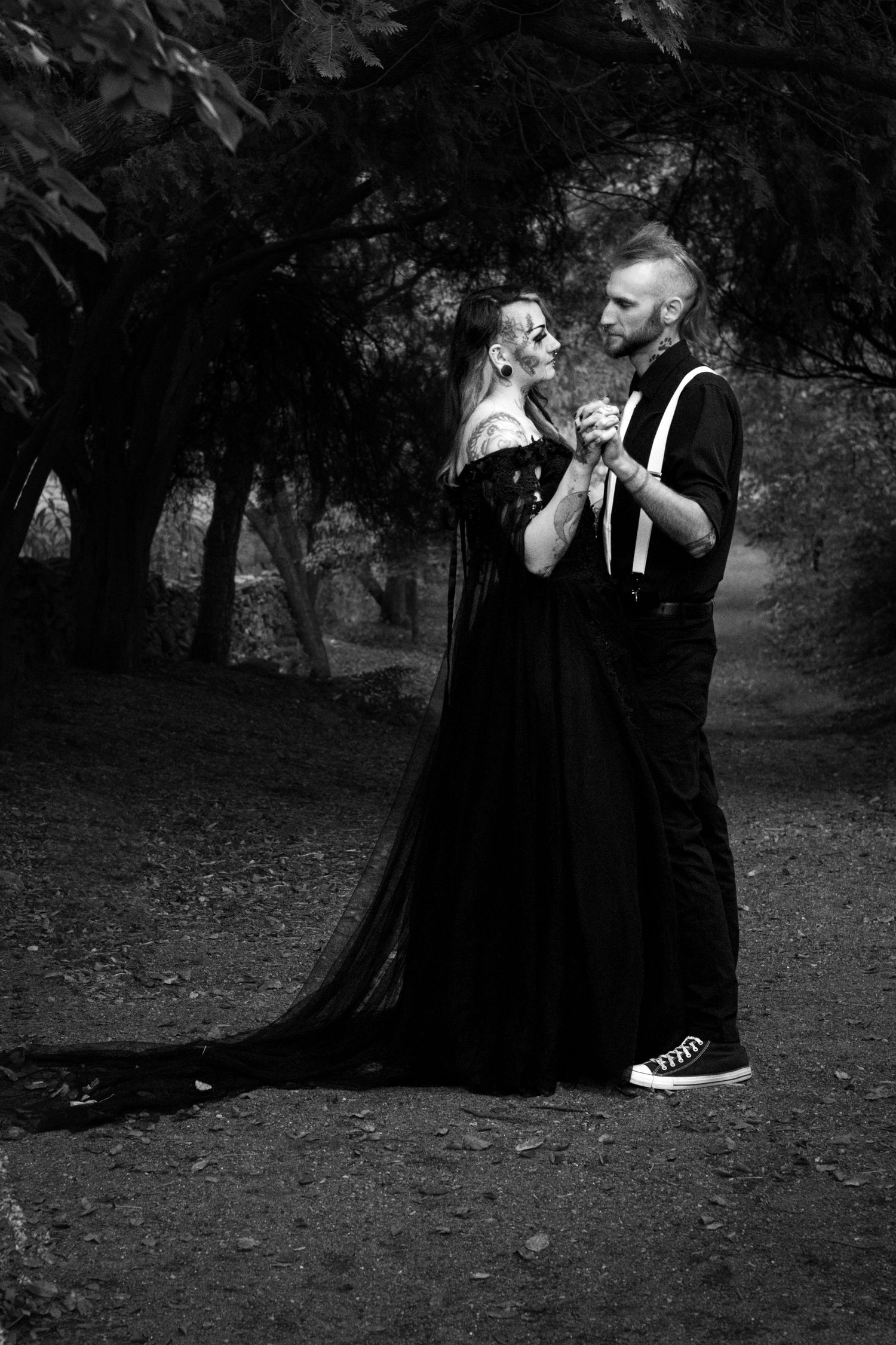 A series of black and white photographs showing two people in dark clothing embracing in a wooded outdoor setting.