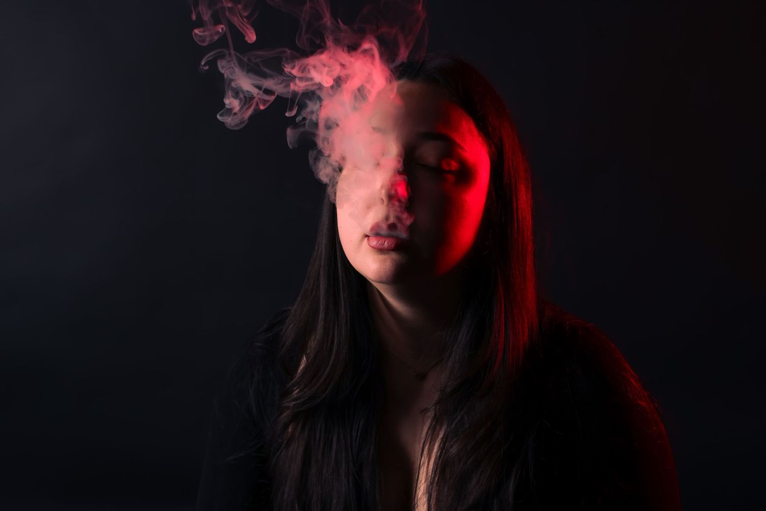 Young woman exhaling smoke under dramatic red light against dark background.