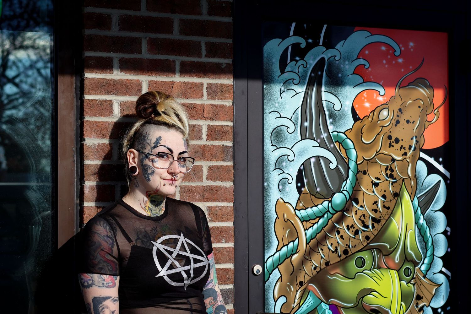 A person in a pentagram t-shirt stands next to colorful street art featuring sea creatures and monsters on a brick wall.