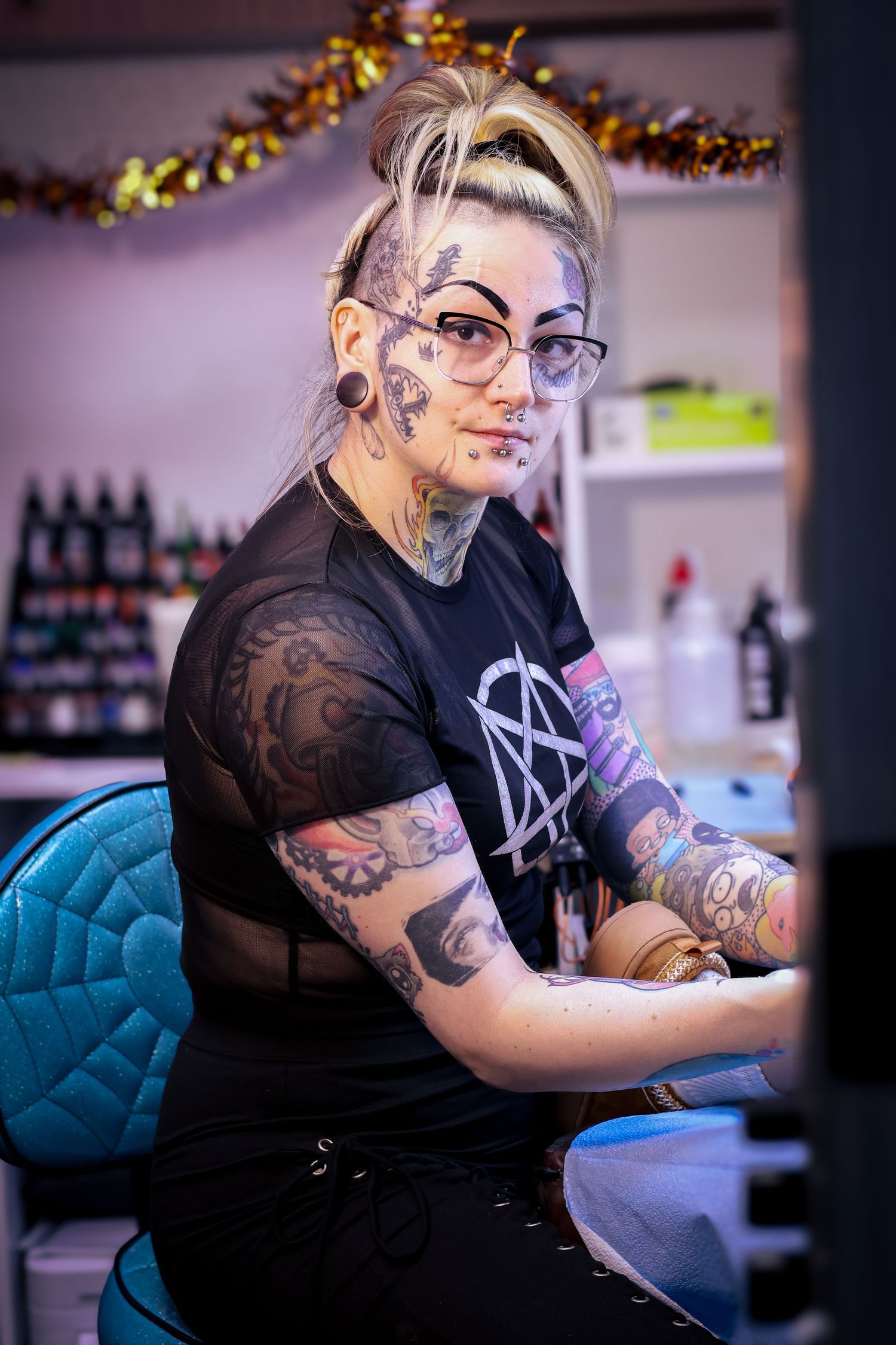 Tattooed artist with glasses concentrating while working at a professional tattoo station.