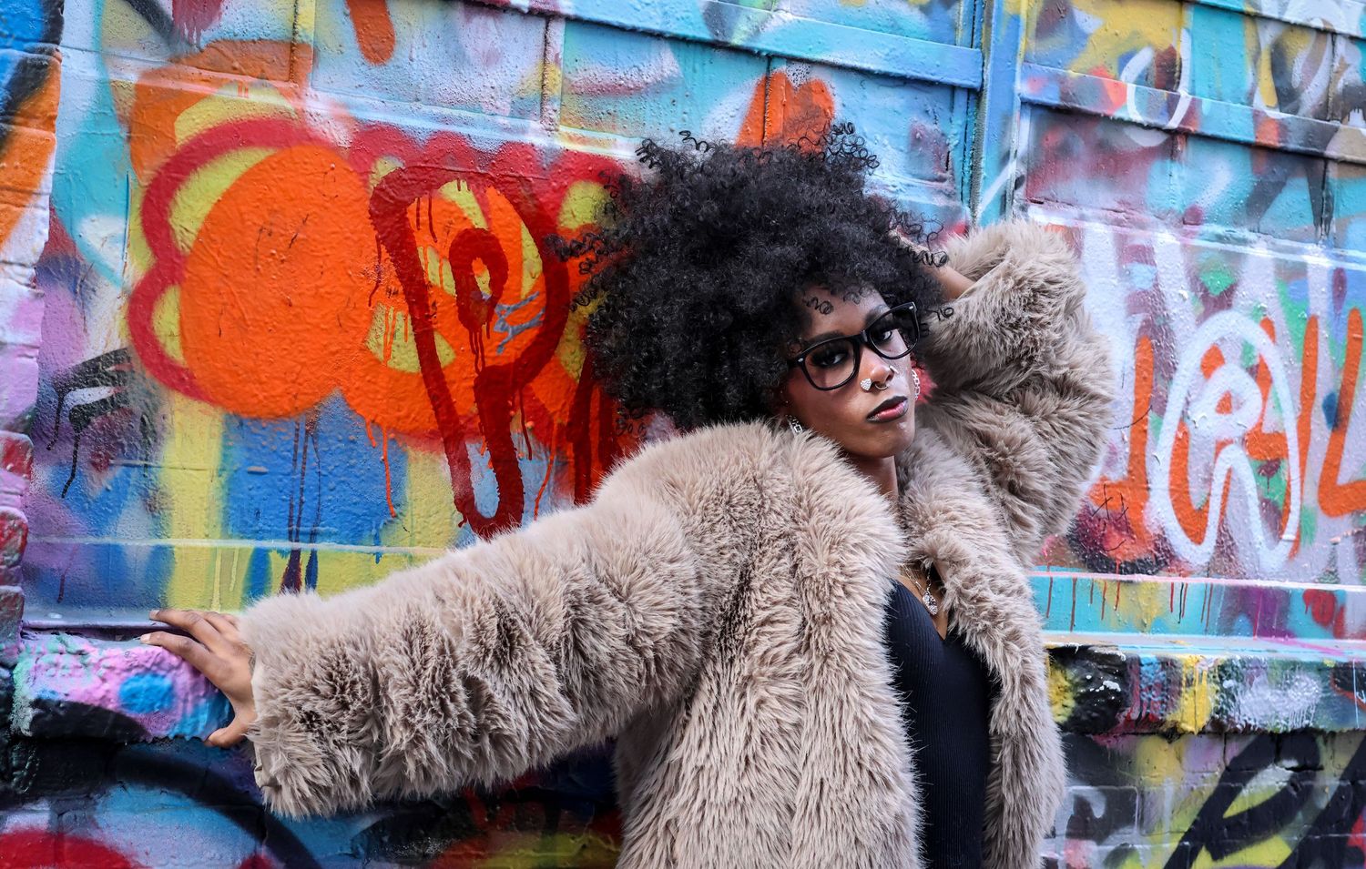 Fashion shoot featuring a brown fuzzy coat against an urban wall with bright graffiti art.