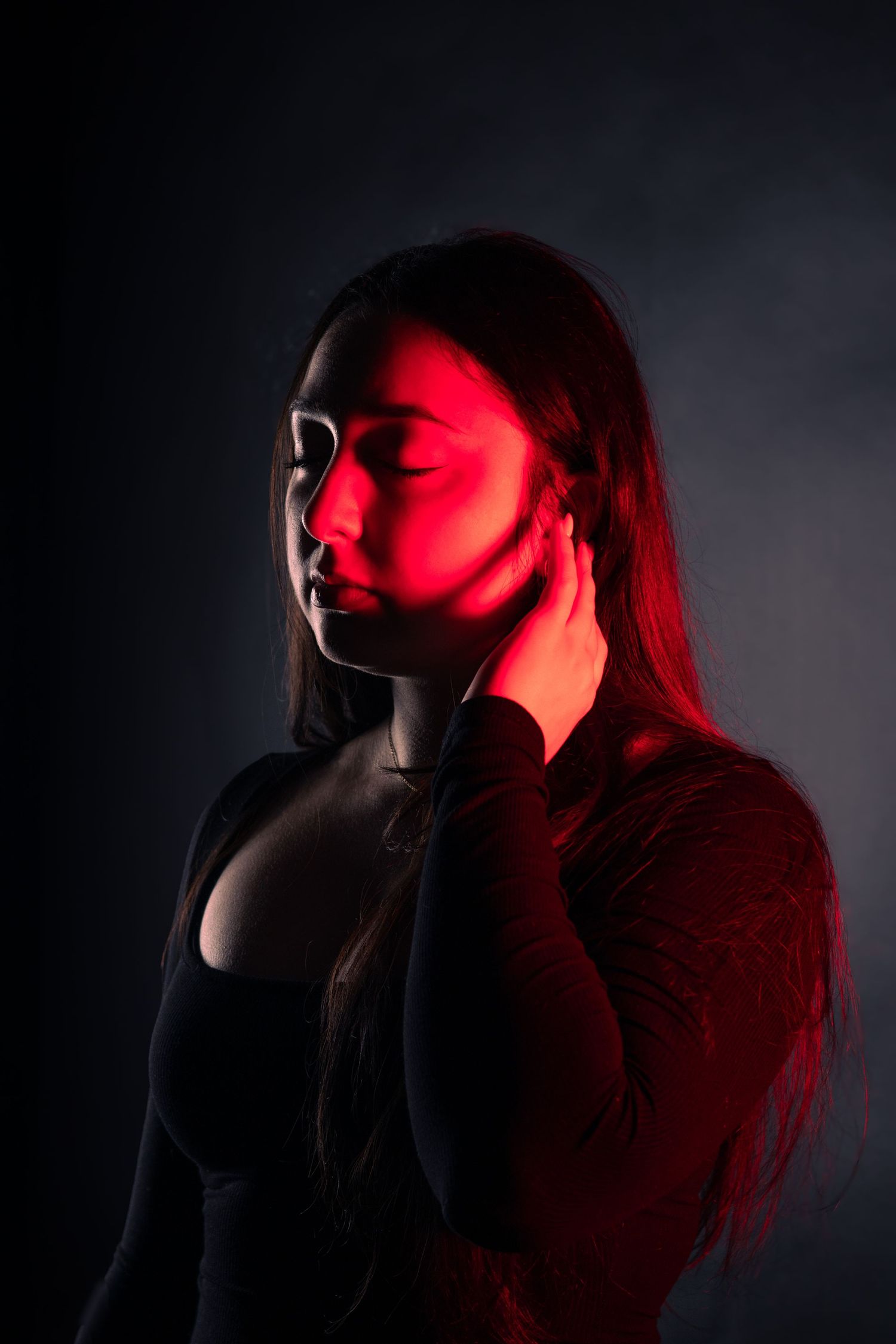 Woman with long hair posed in profile with red dramatic lighting against dark background.