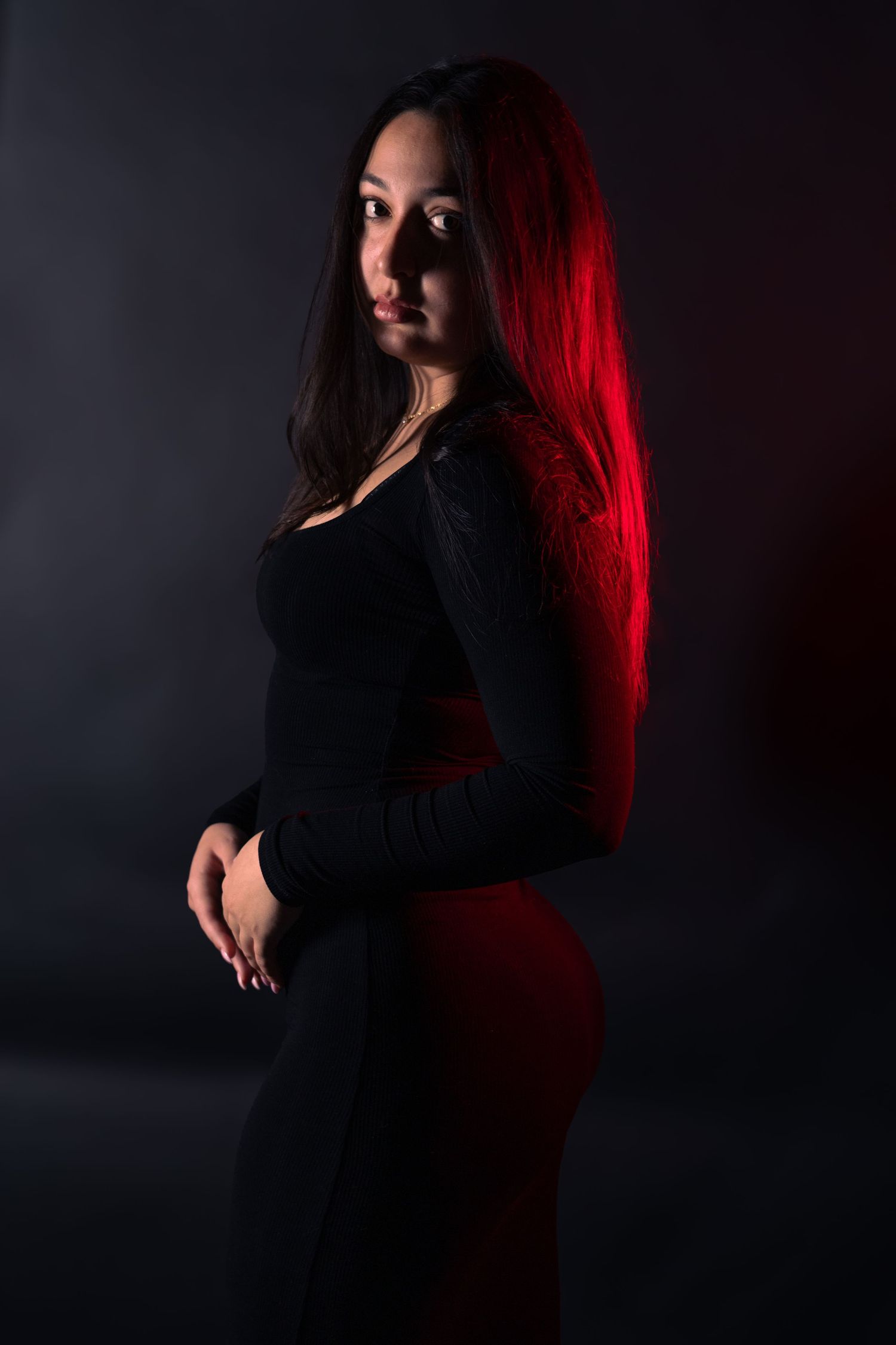 Young woman in black top and red skirt posing with vibrant red hair under moody lighting.