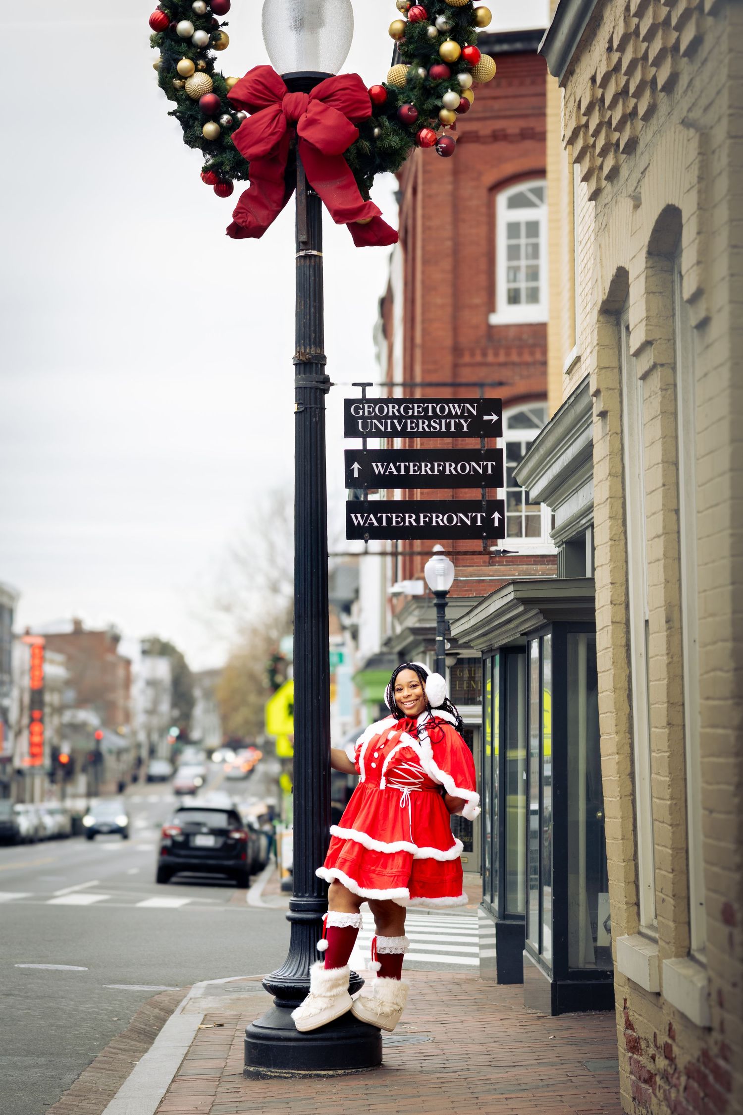 Woman in red Mrs. Claus costume poses by decorated lamppost near Georgetown University sign in Washington DC.