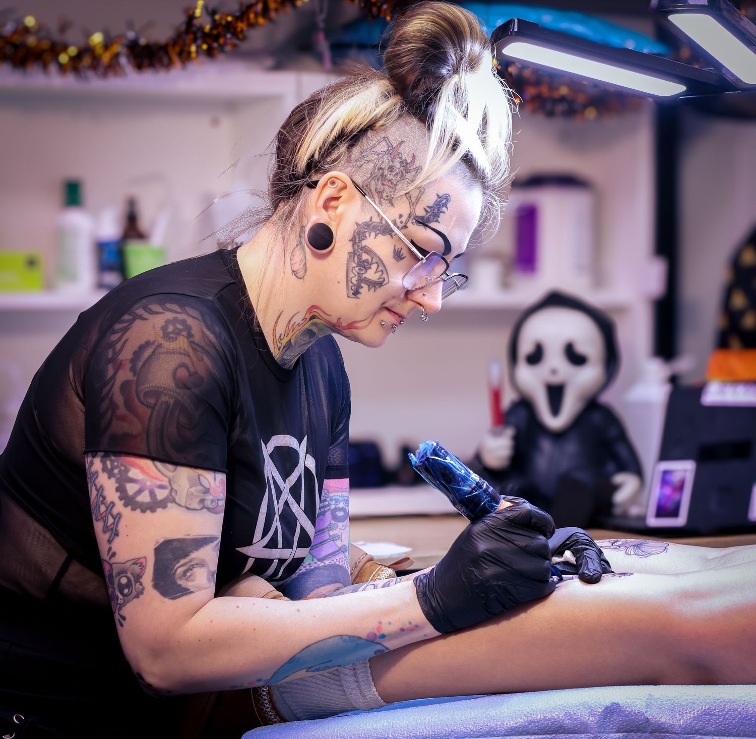 A tattoo artist works meticulously on a client's arm in a professional studio with bright lighting and modern equipment.