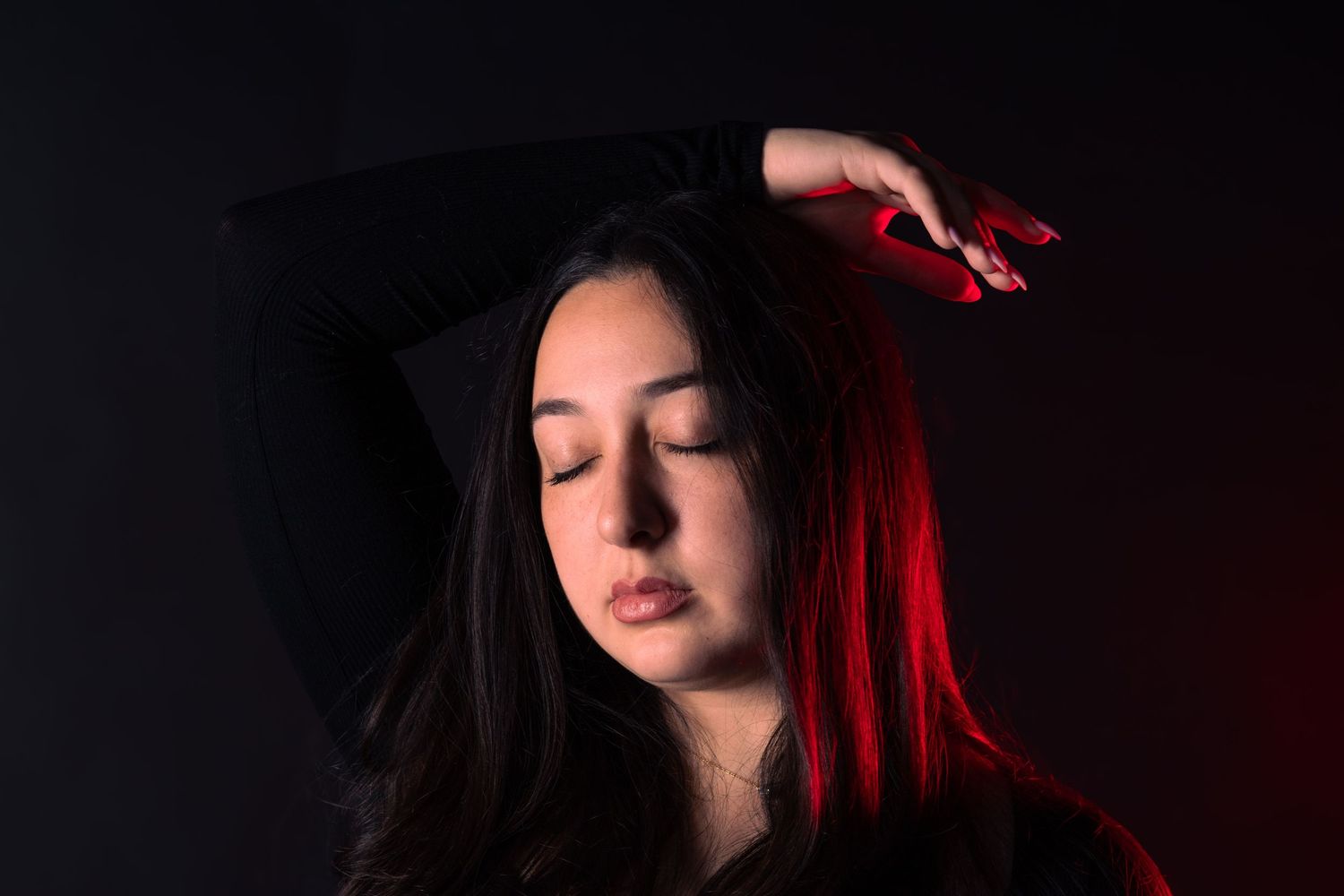 Young woman with red-highlighted hair posing with eyes closed in dark studio.