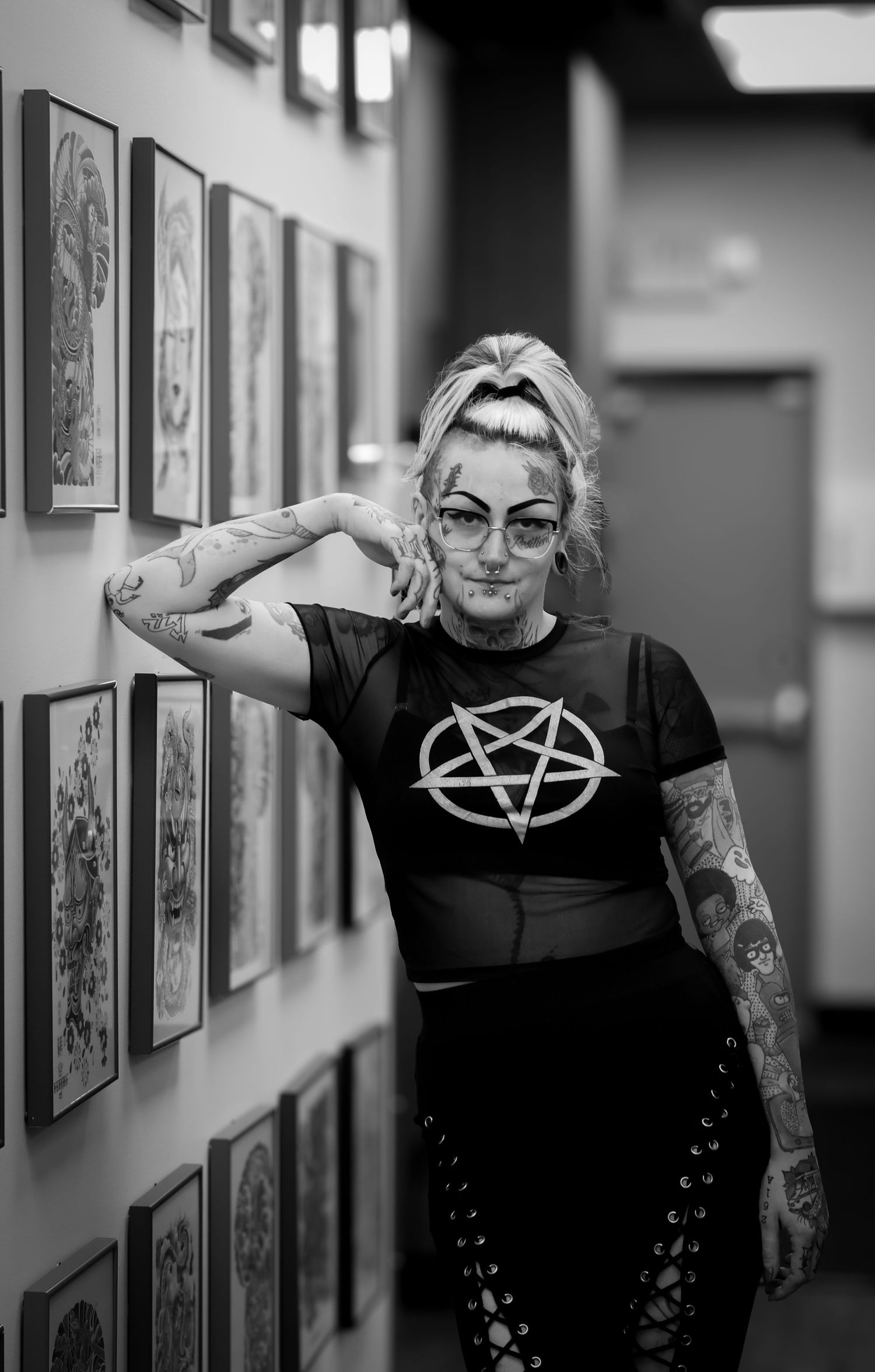 A black and white photo series showing a person in a pentagram t-shirt posing against a wall with framed artwork.