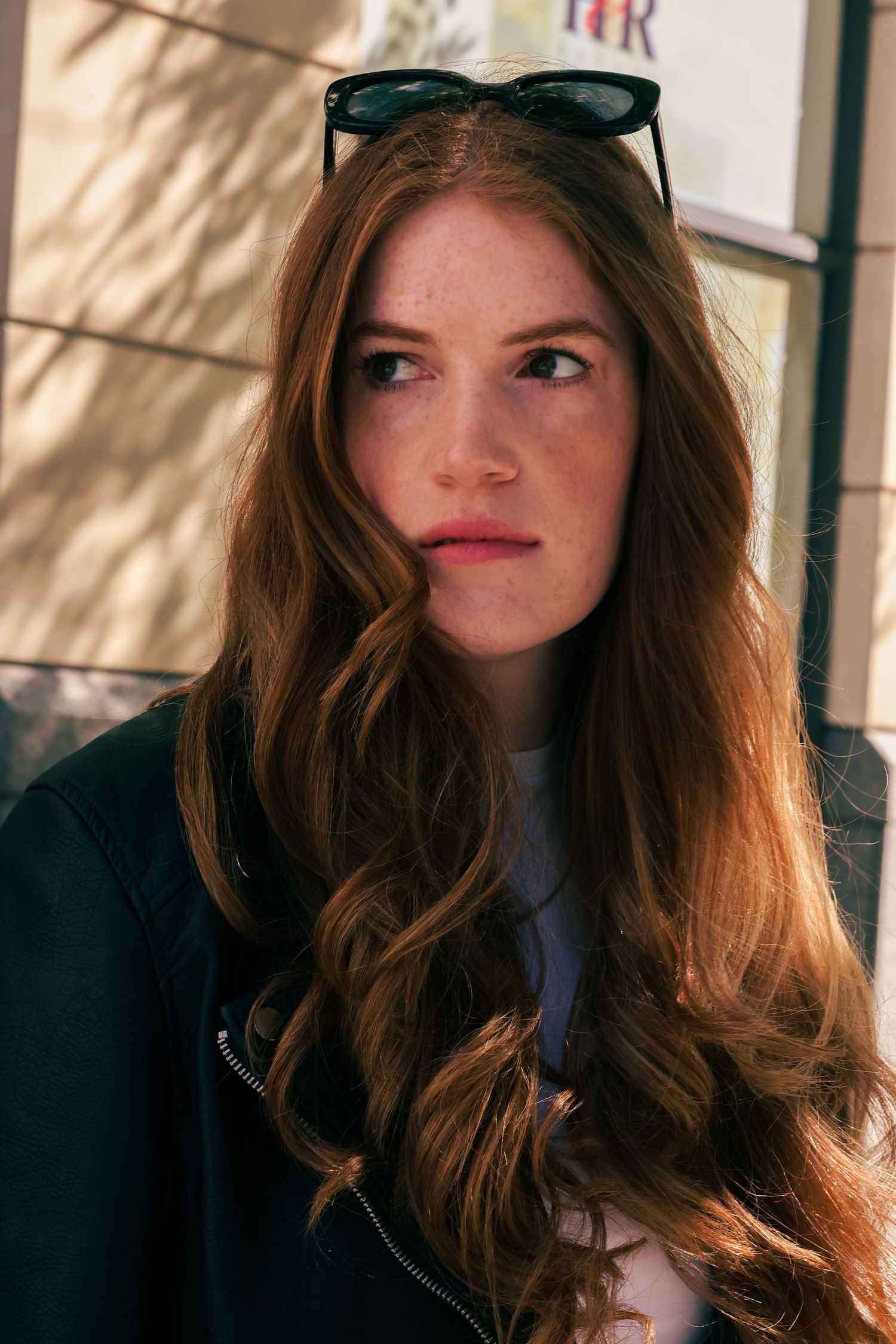 Close-up of freckled redhead woman with wavy hair and sunglasses on head in natural sunlight outdoors.