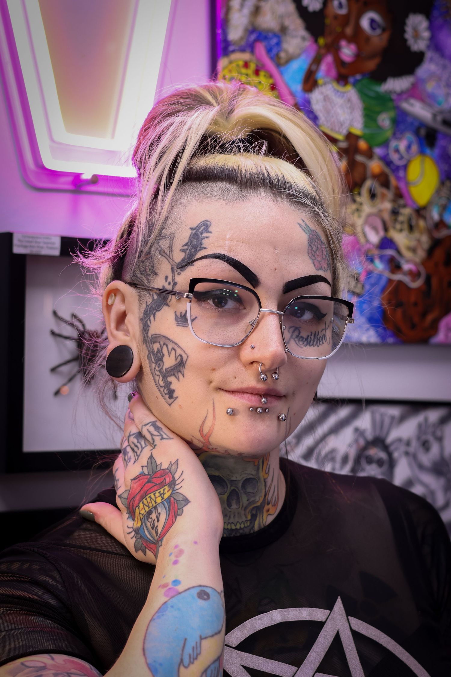 A person with facial tattoos and glasses poses in multiple shots against a colorful background.