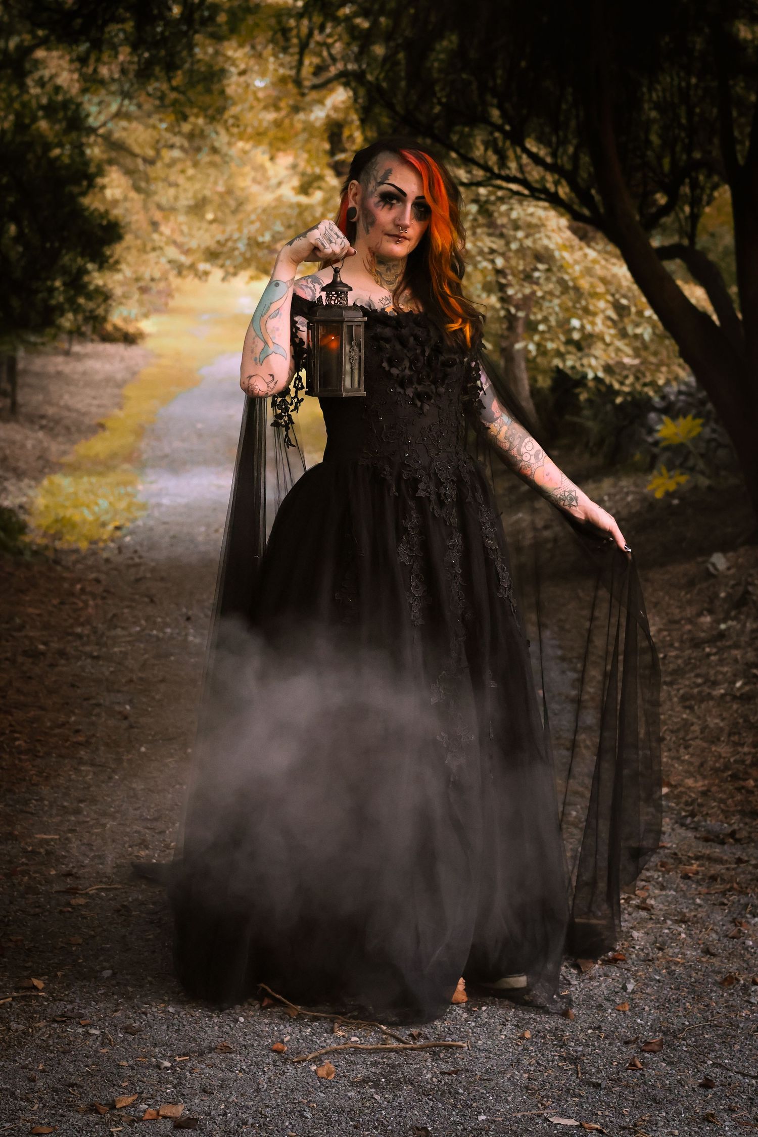 A figure in a flowing black dress poses dramatically on a misty forest path during autumn.
