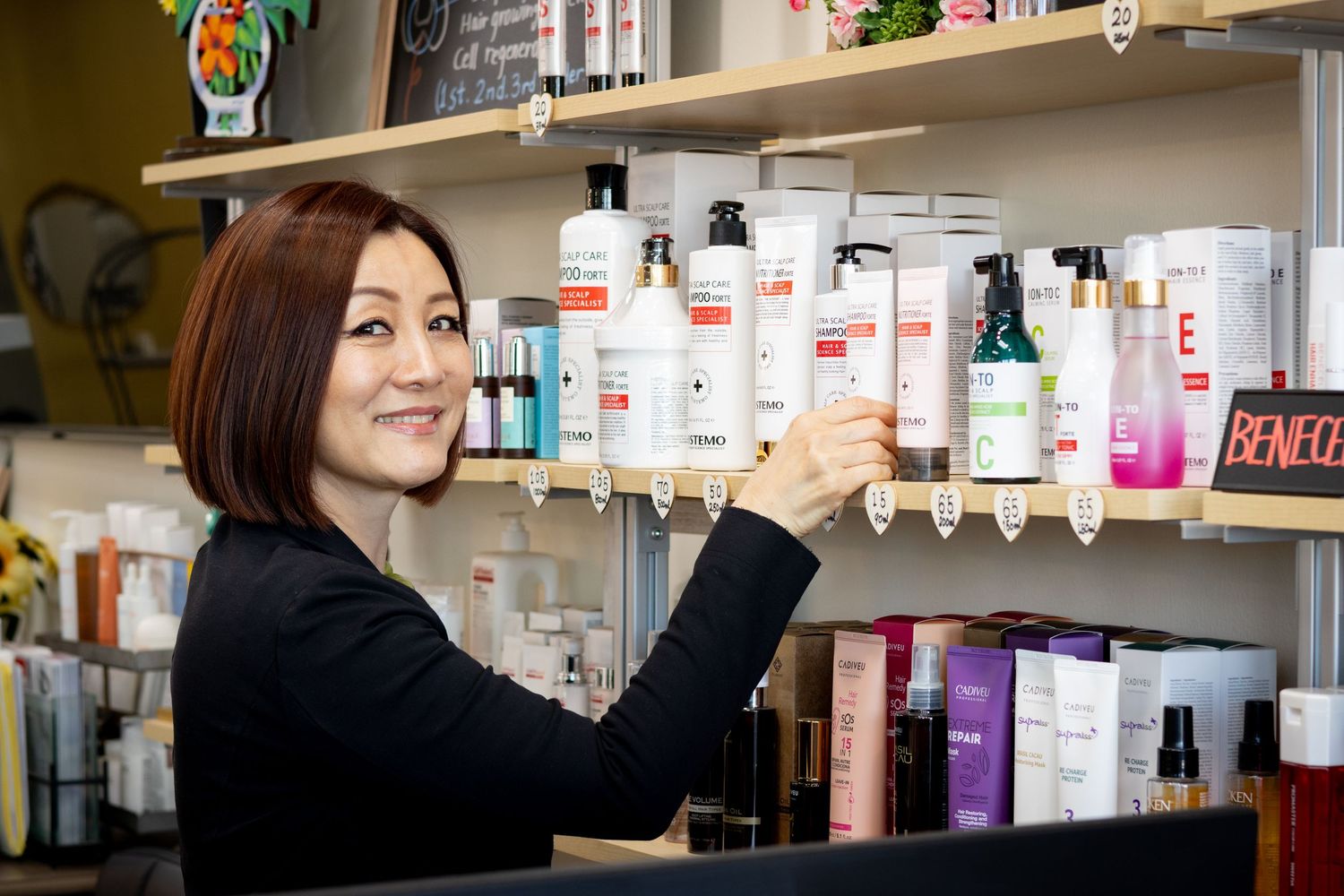 A beauty store employee reaches for hair care products displayed on white shelving units.
