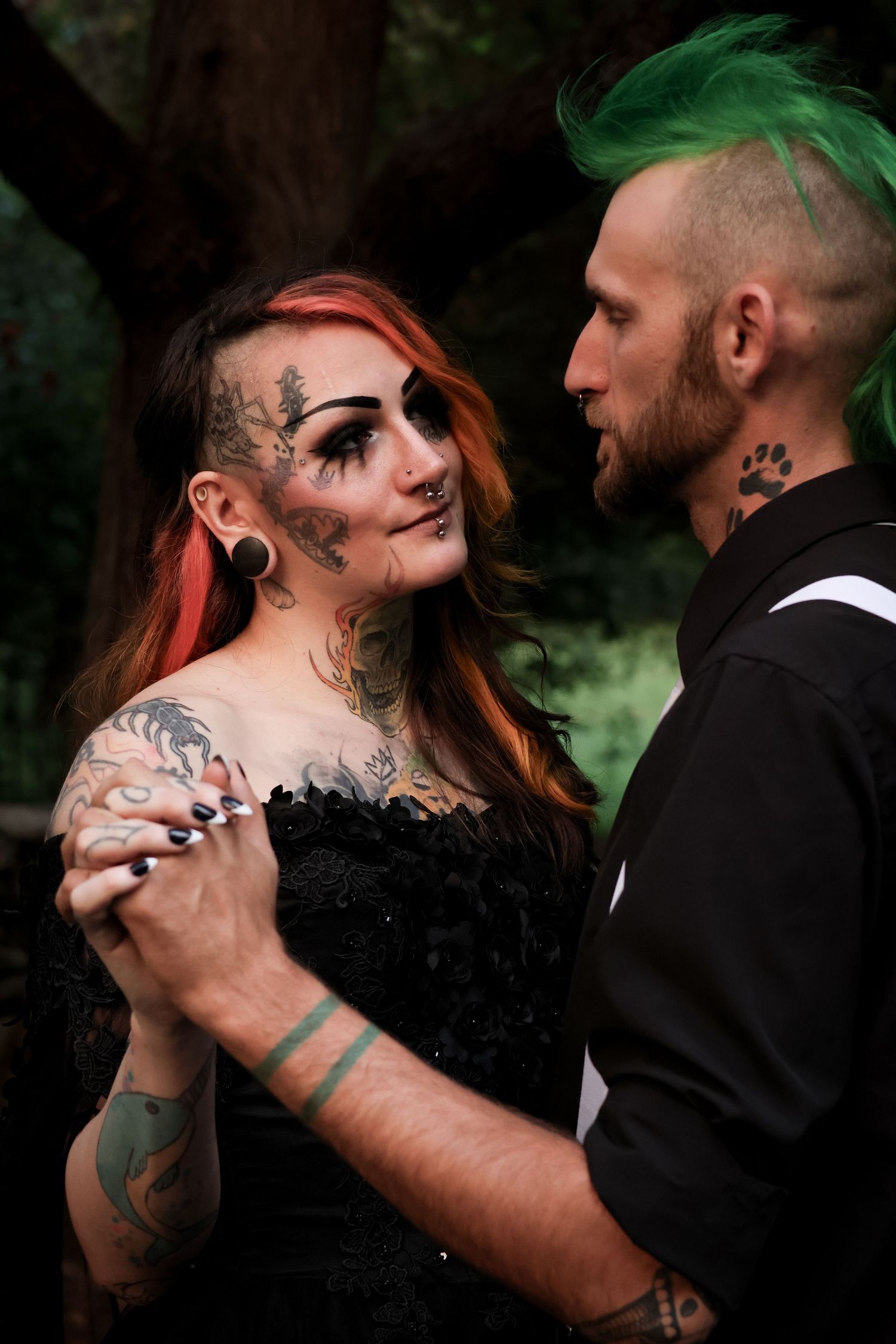 A couple in gothic wedding attire share an intimate moment against a dark forest backdrop.