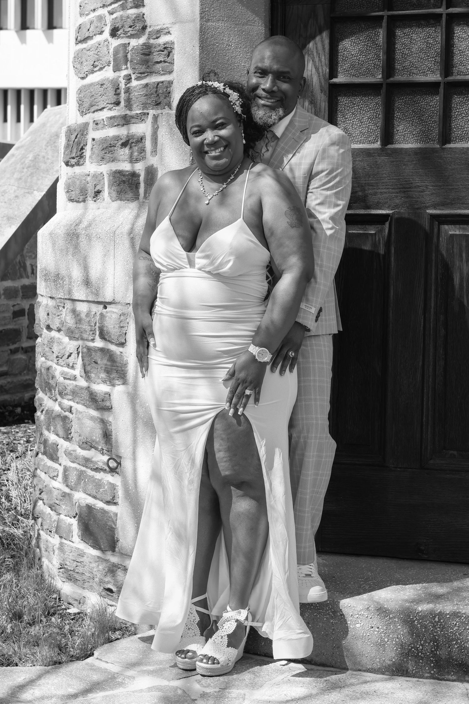 Black and white photo of couple posing together by stone building entrance.