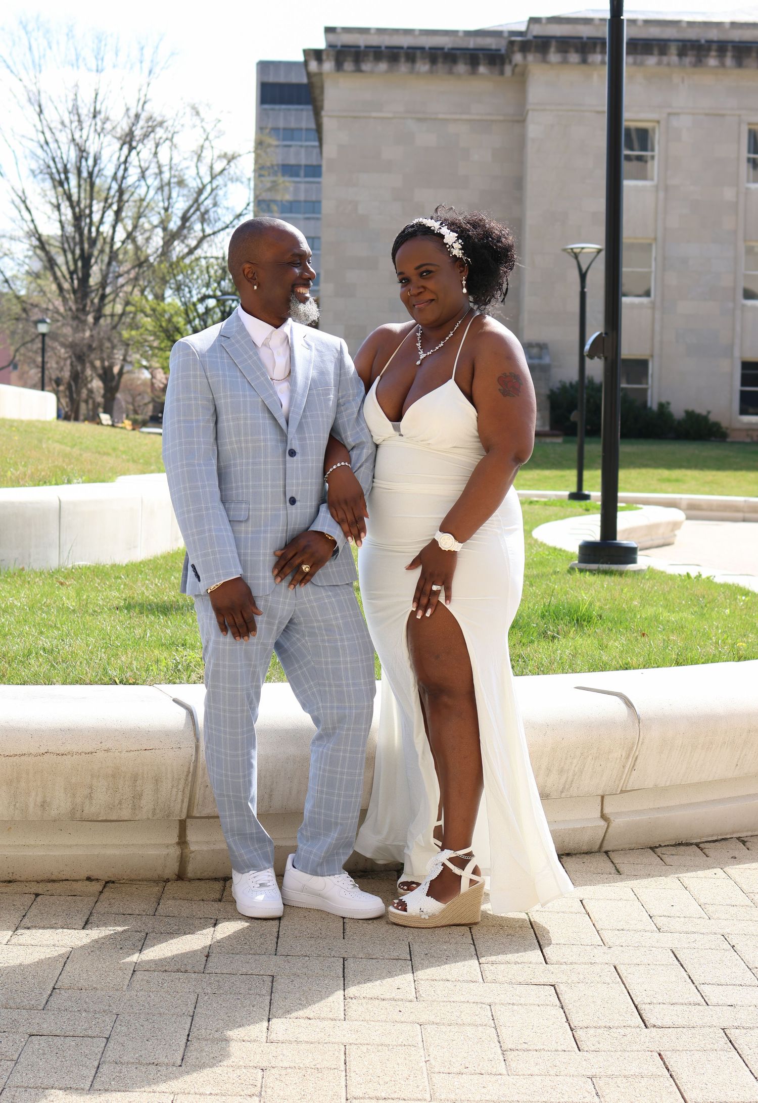 Couple in wedding attire posing together on a sunny outdoor patio.